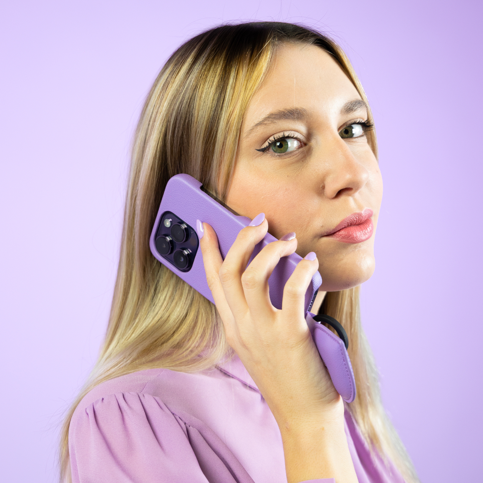 Donna bionda in viola parla al telefono con custodia coordinata su sfondo viola.