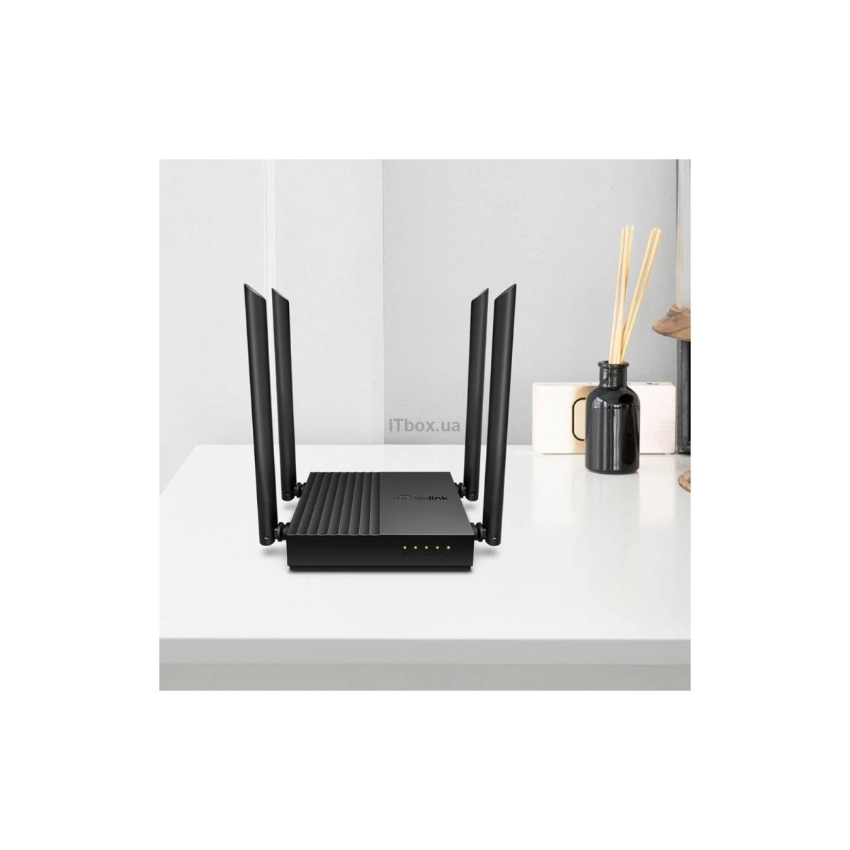 Ein schwarzer WLAN-Router mit vier vertikalen Antennen steht auf einem weißen Tisch vor einer grauen Wand.