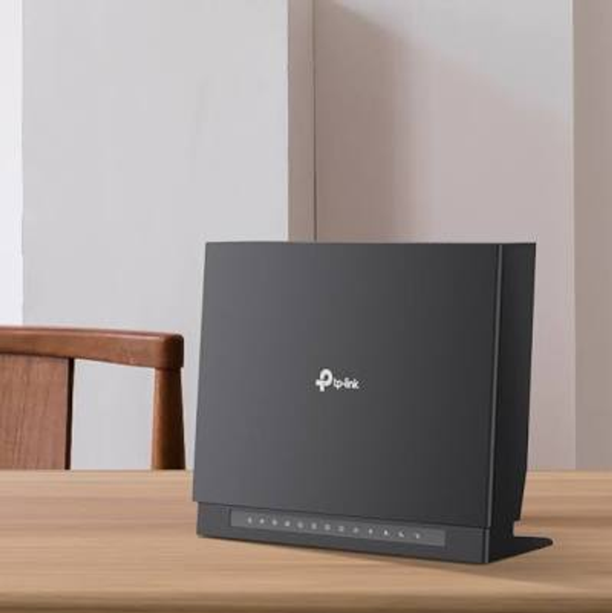 Ein schwarzer TP-Link WLAN-Router steht auf einem Holztisch vor einer weißen Wand, daneben ein Holzstuhl.