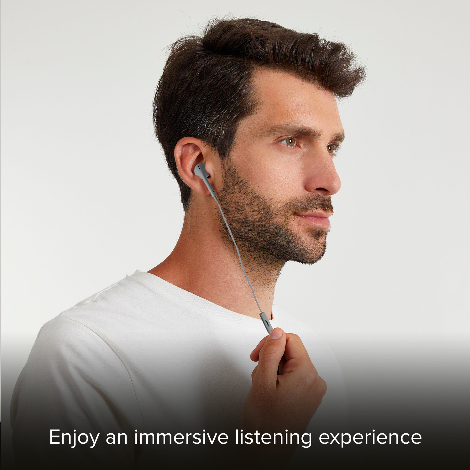 Un uomo indossa auricolari bianchi e tiene il cavo davanti a uno sfondo grigio.