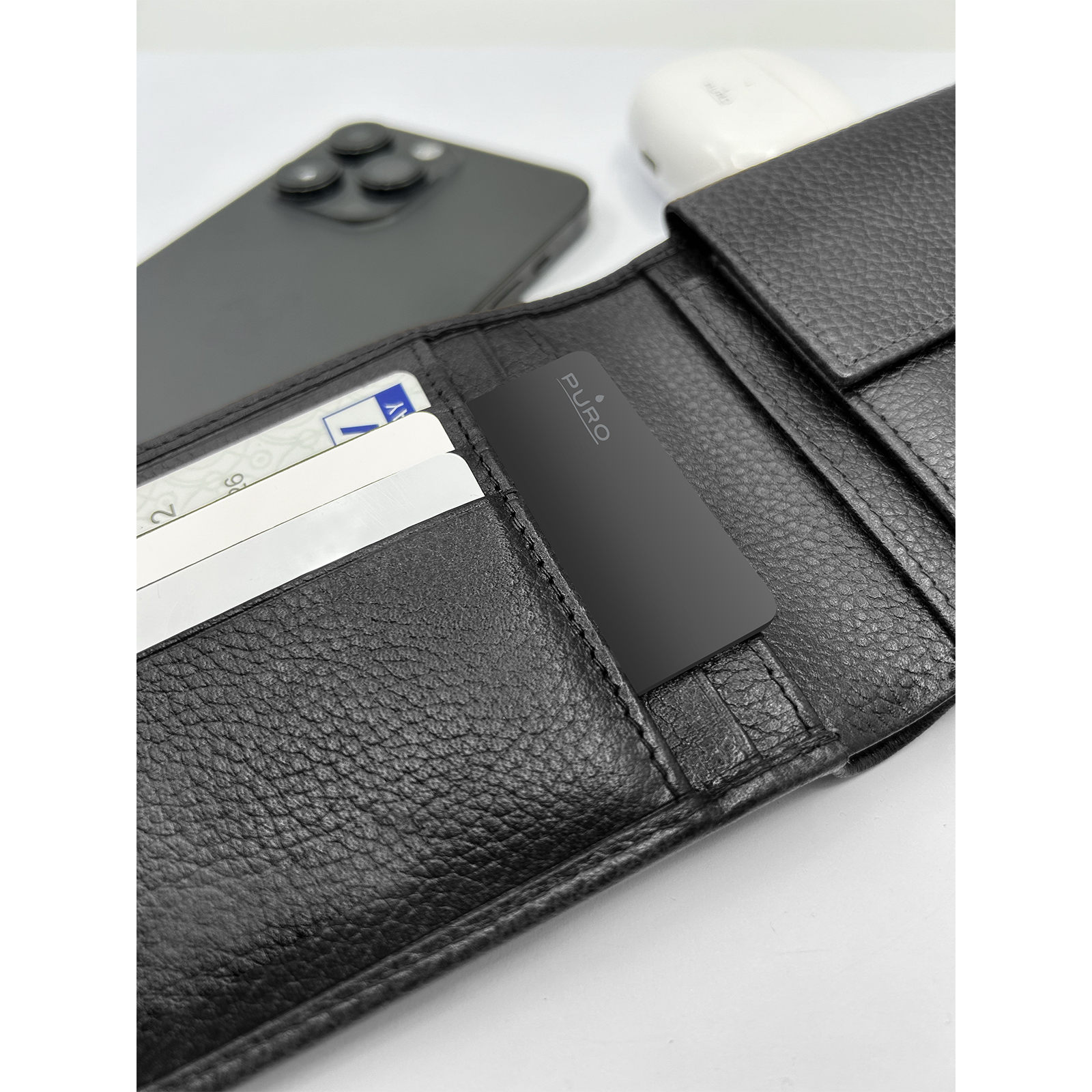 Cartera de cuero negro abierta con tarjetas, una tarjeta rastreadora Puro negra, smartphone y auriculares.