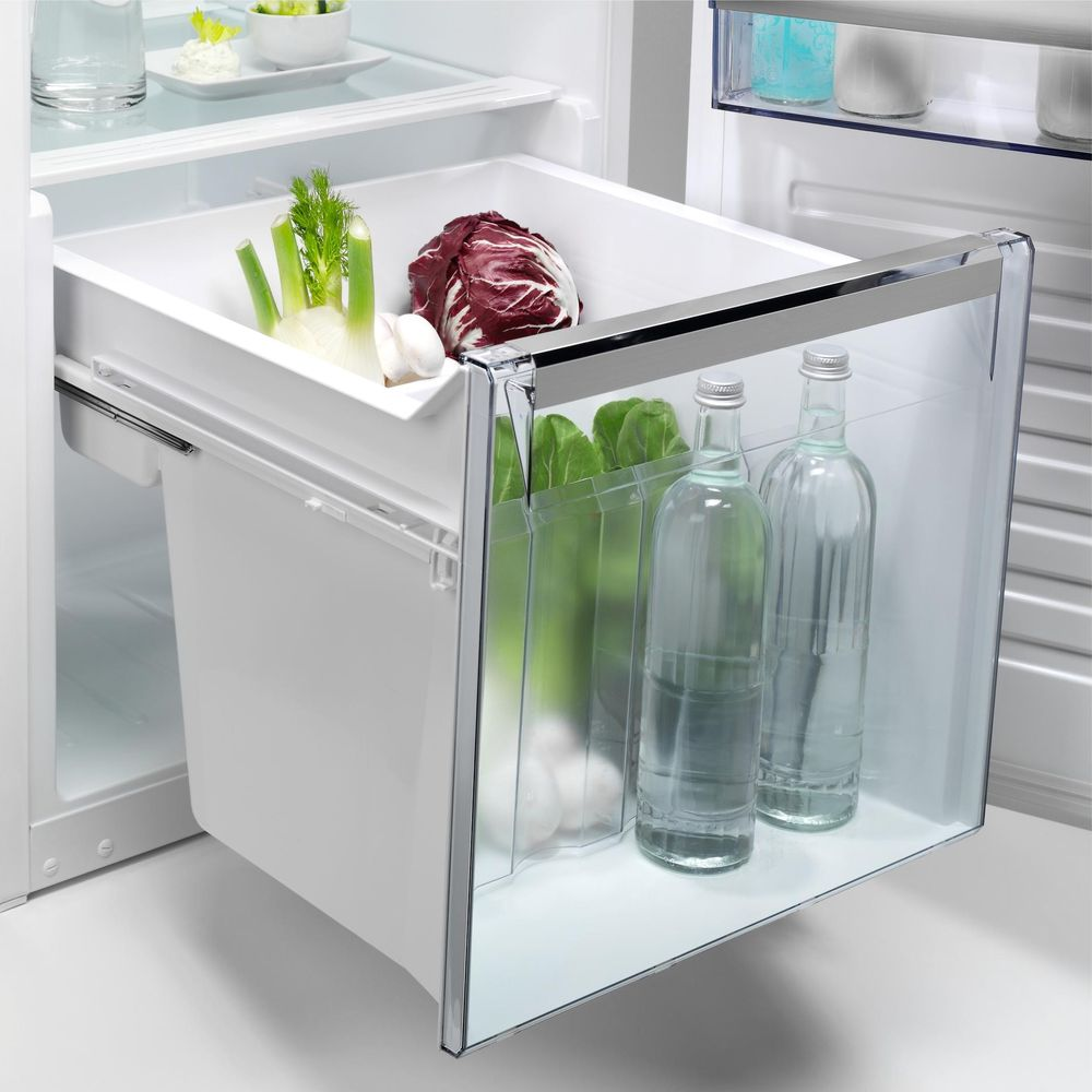 Un cassetto del frigorifero aperto contiene verdure, radicchio e due bottiglie d'acqua.