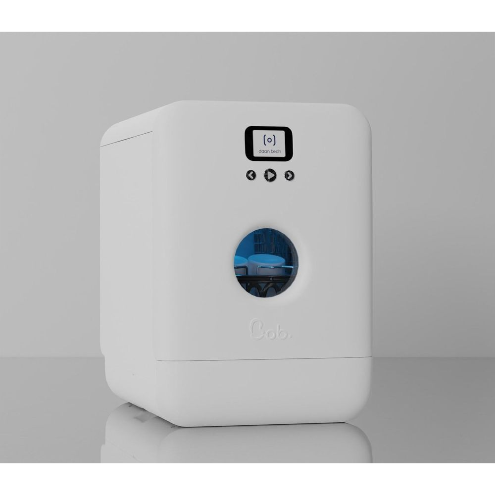 Una lavastoviglie compatta bianca con finestra rotonda illuminata di blu e display digitale su superficie grigia.