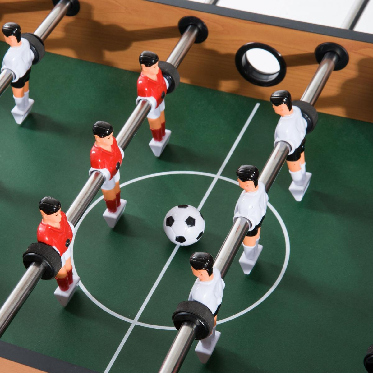 Ein Kicker mit grünem Spielfeld, weißen Markierungen, kleinem Ball in der Mitte und rot-weißen Spielfiguren.