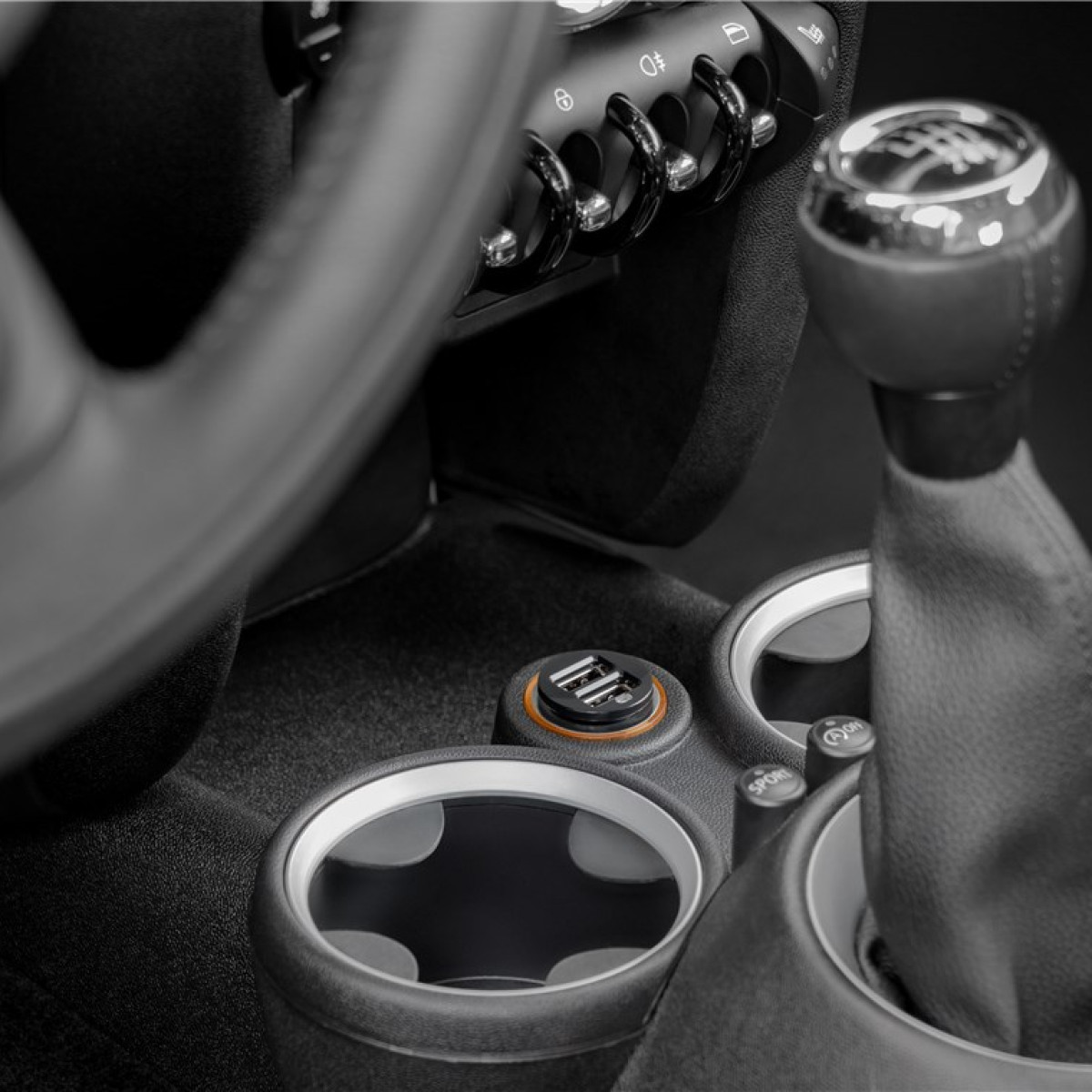 Nahaufnahme des Autoinnenraums mit Schalthebel, Becherhaltern und USB-Anschluss in Schwarz-Weiß.
