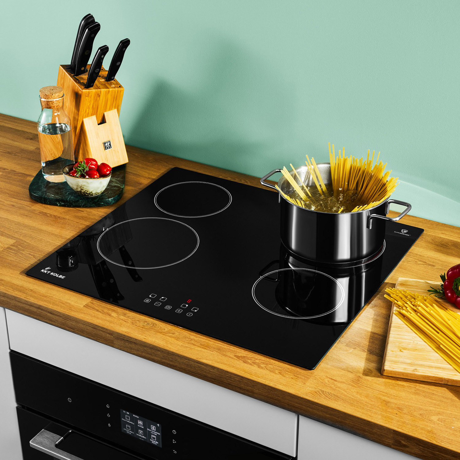 Una pentola di spaghetti cuoce su un piano cottura a induzione nero su un piano di lavoro in legno.