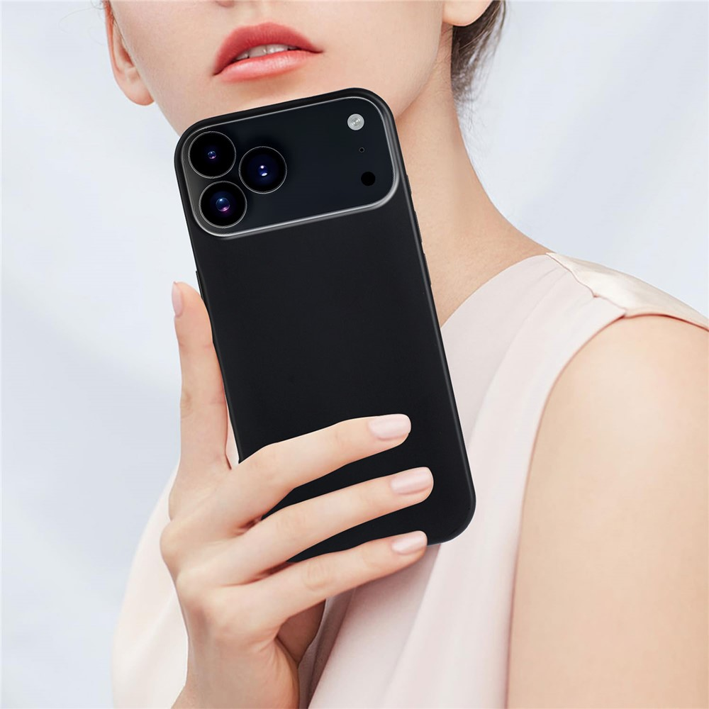 Eine Frau hält ein schwarzes Smartphone mit dreifacher Kamera in der Hand vor ihrem Gesicht.