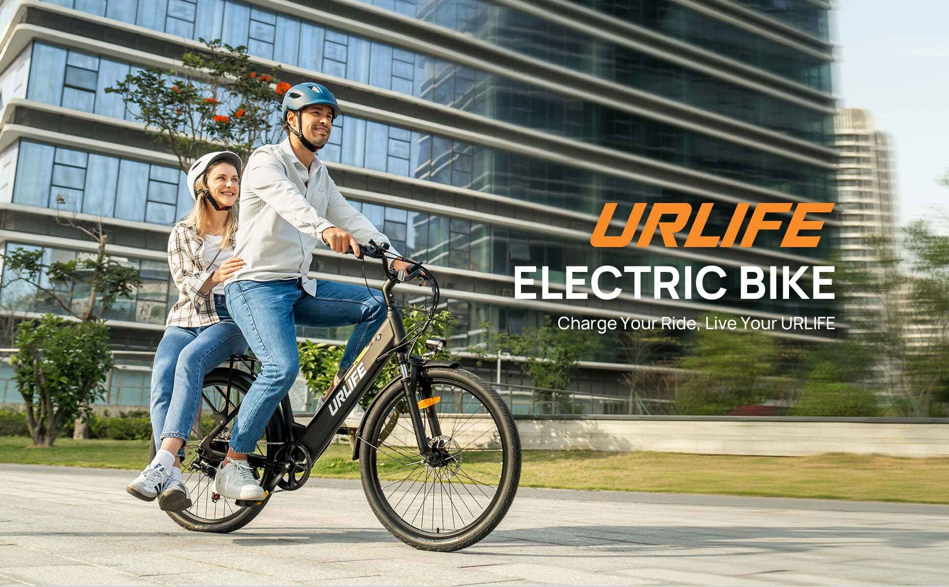 Un uomo e una donna guidano una bici elettrica davanti a un edificio moderno.