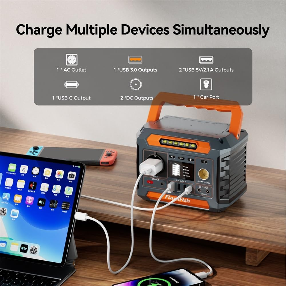 Una estación de energía portátil gris con asa naranja carga una tableta y un teléfono en una mesa de madera.