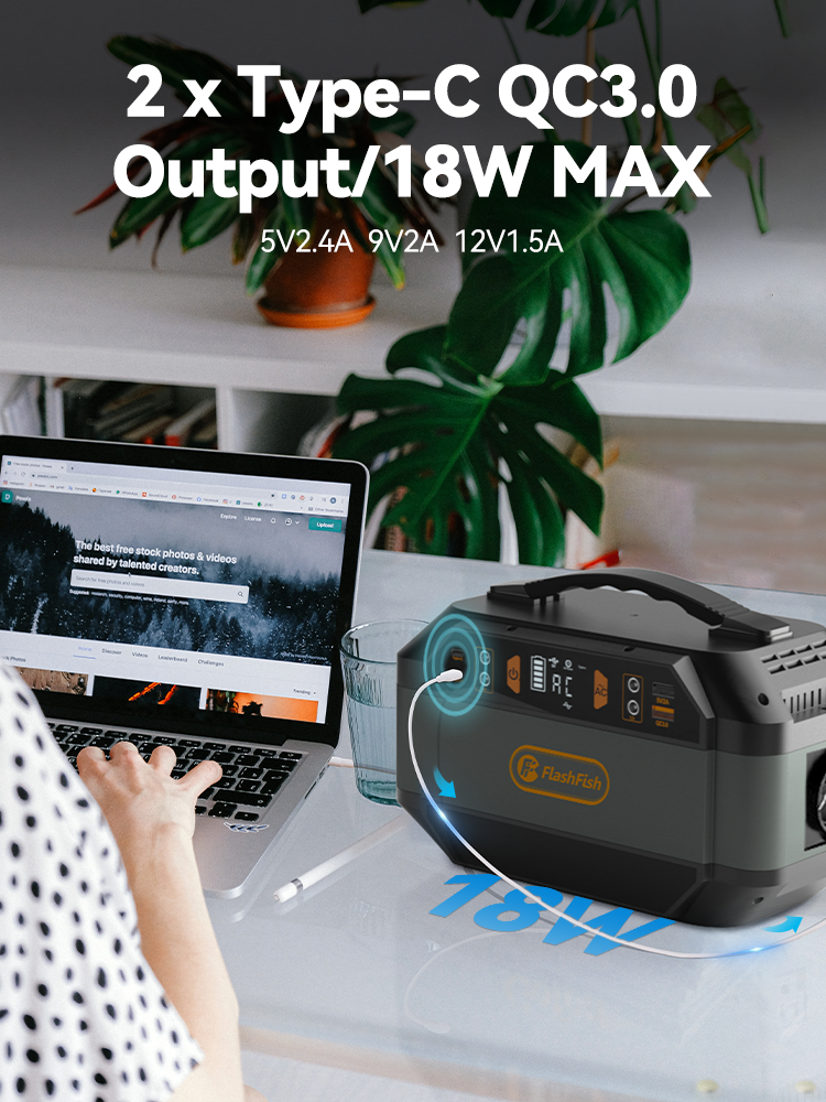 Una estación de energía portátil en un escritorio carga un dispositivo por USB-C, con un portátil de fondo.