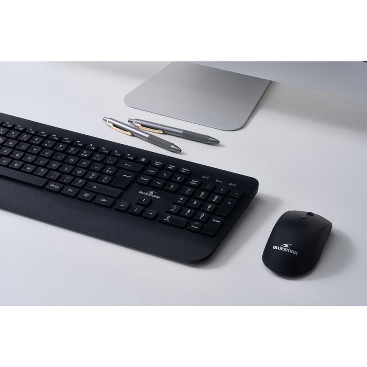 Una tastiera nera, un mouse per computer e due penne su una scrivania bianca.