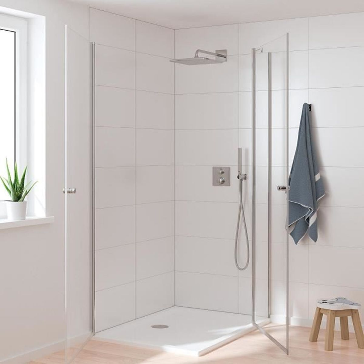Moderne Dusche mit Glastüren, weißen Fliesen, hängendem Handtuch und einem kleinen Holzschemel im hellen Badezimmer.