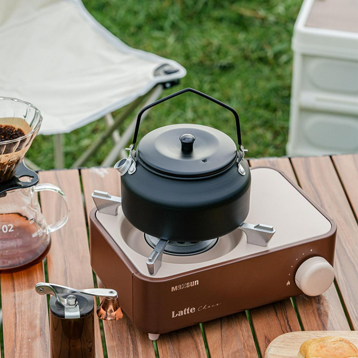 Ein schwarzer Teekessel auf einem braunen Gaskocher im Freien auf einem Holzschreibtisch mit Kaffeebereiter.