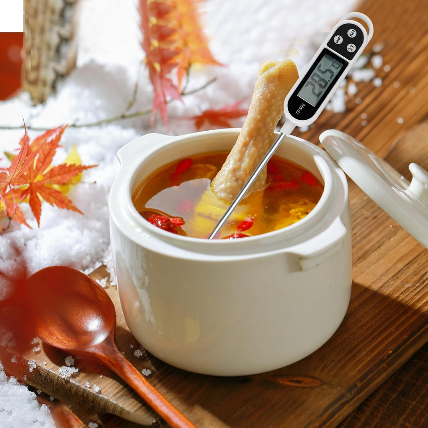 Ein Fleischthermometer misst die Temperatur einer Hühnersuppe in einer weißen Schüssel auf Holz.