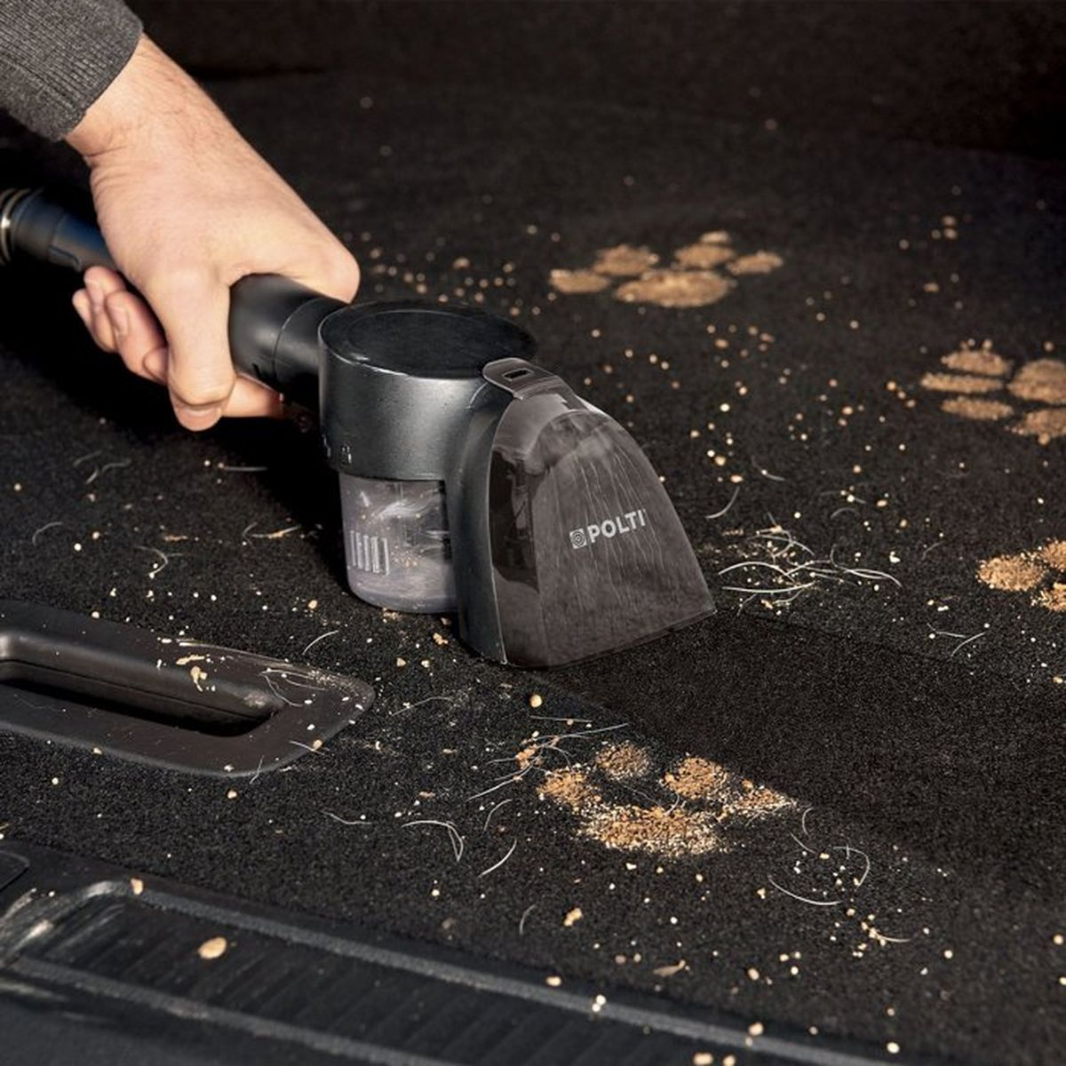 Eine Hand reinigt schwarzen Autoteppich mit einem Polti-Staubsauger und entfernt Schmutz und Tierhaare.