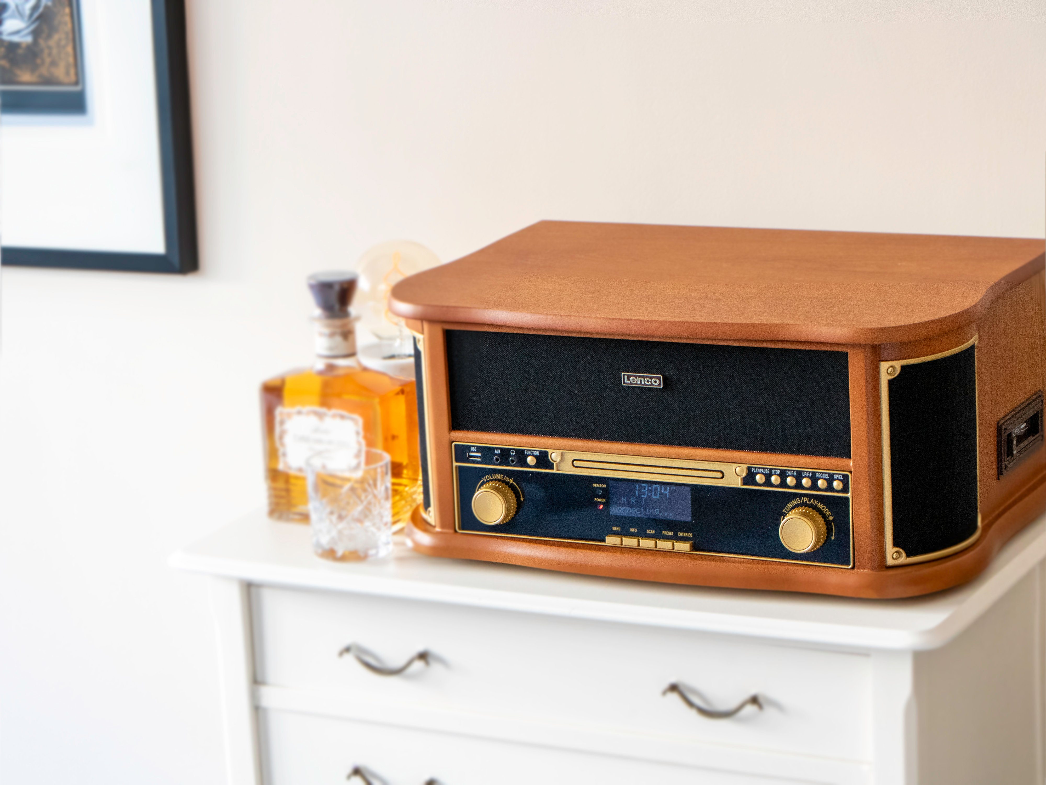 Ein vintage Lenco-Musiksystem aus Holz steht auf einer weißen Kommode neben einer Schnapsflasche und einem Glas.