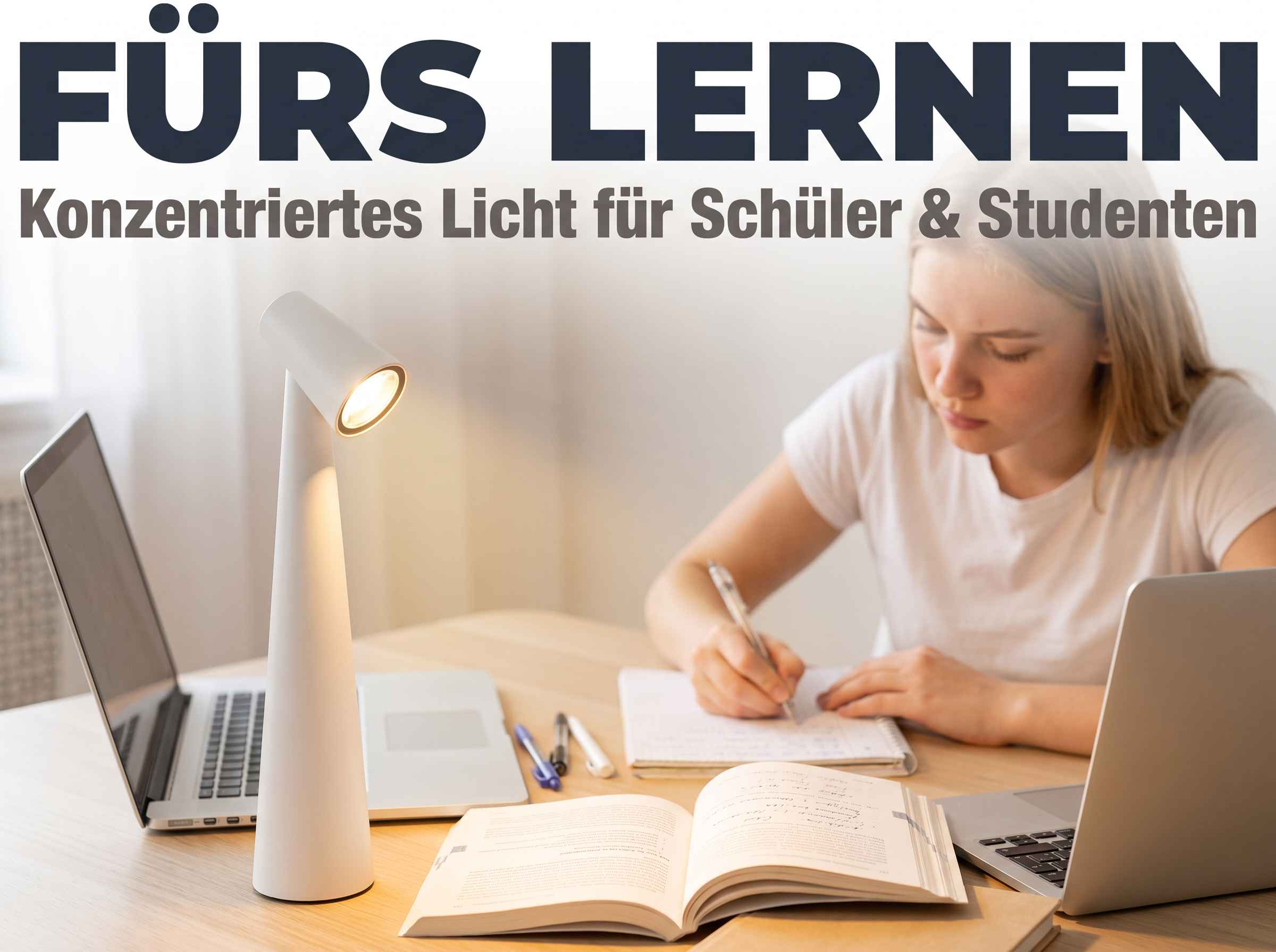 Eine junge Frau lernt an einem Schreibtisch mit zwei Laptops, Heften und einer weißen Tischlampe.