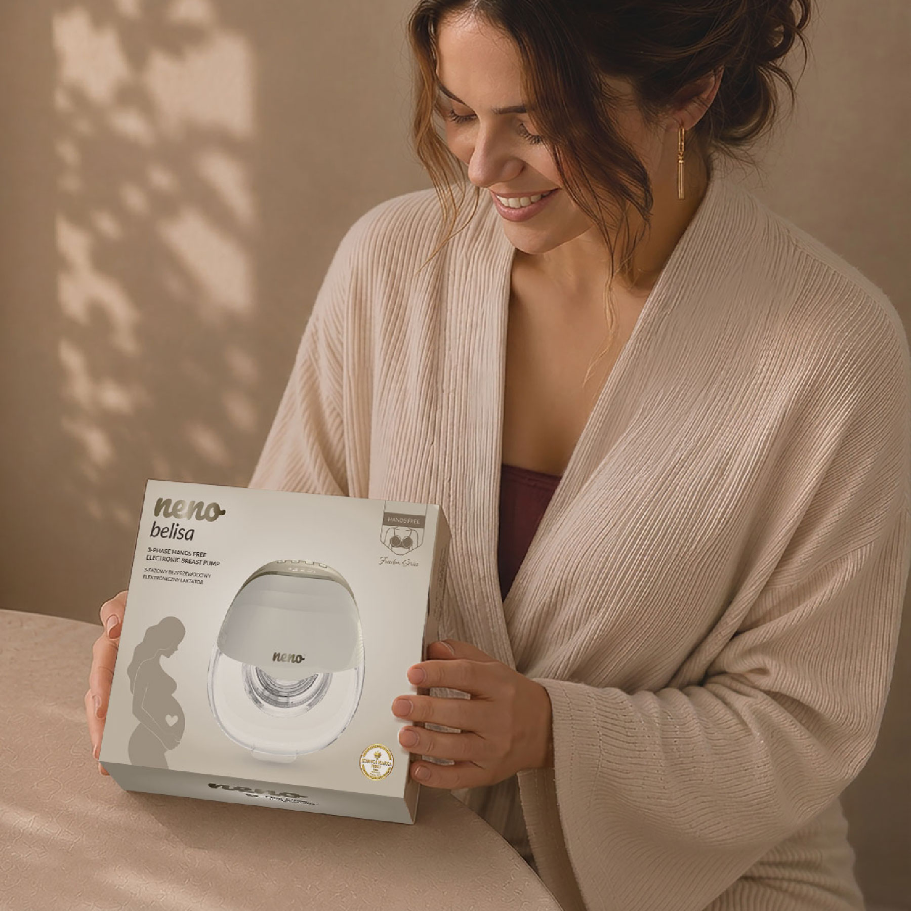 Eine smiling Frau in beiger Robe hält eine weiße Neno Belisa Milchpumpe Box in den Händen.