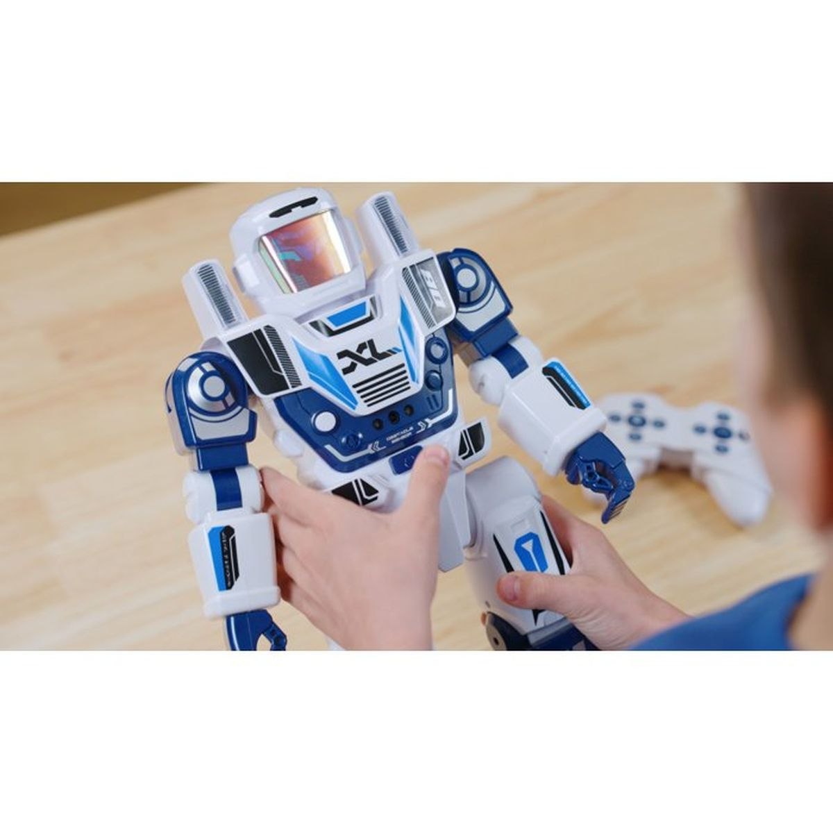 Ein Kind hält einen blau-weißen Roboter auf einem Holztisch, eine Fernbedienung liegt im Hintergrund.