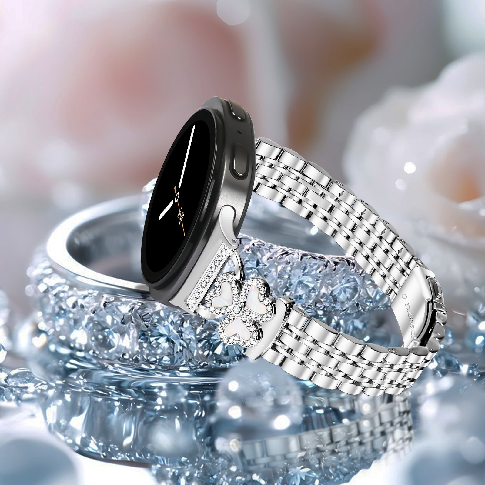 Eine silberne Smartwatch mit kleeblattförmigem Kristall-Charm am Metallarmband auf glitzernder Oberfläche.