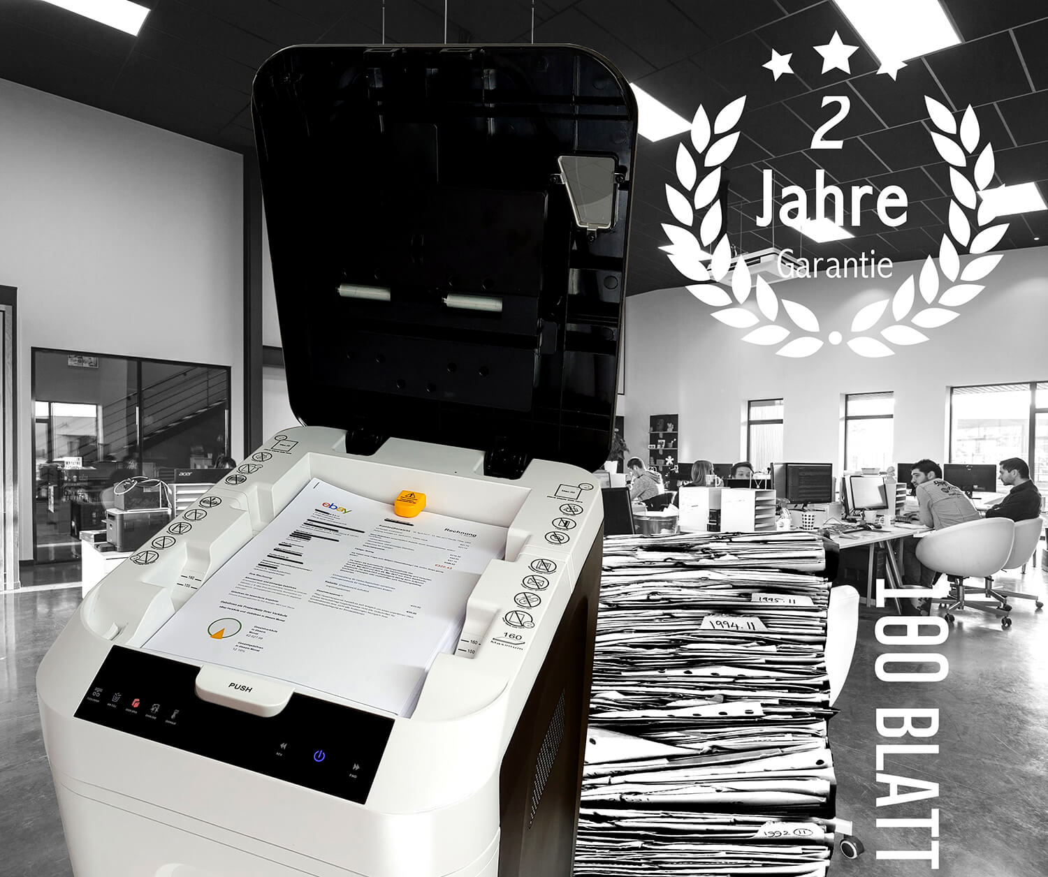 Dokumentenscanner im Vordergrund, dahinter ein Großraumbüro und ein großer Papierstapel.