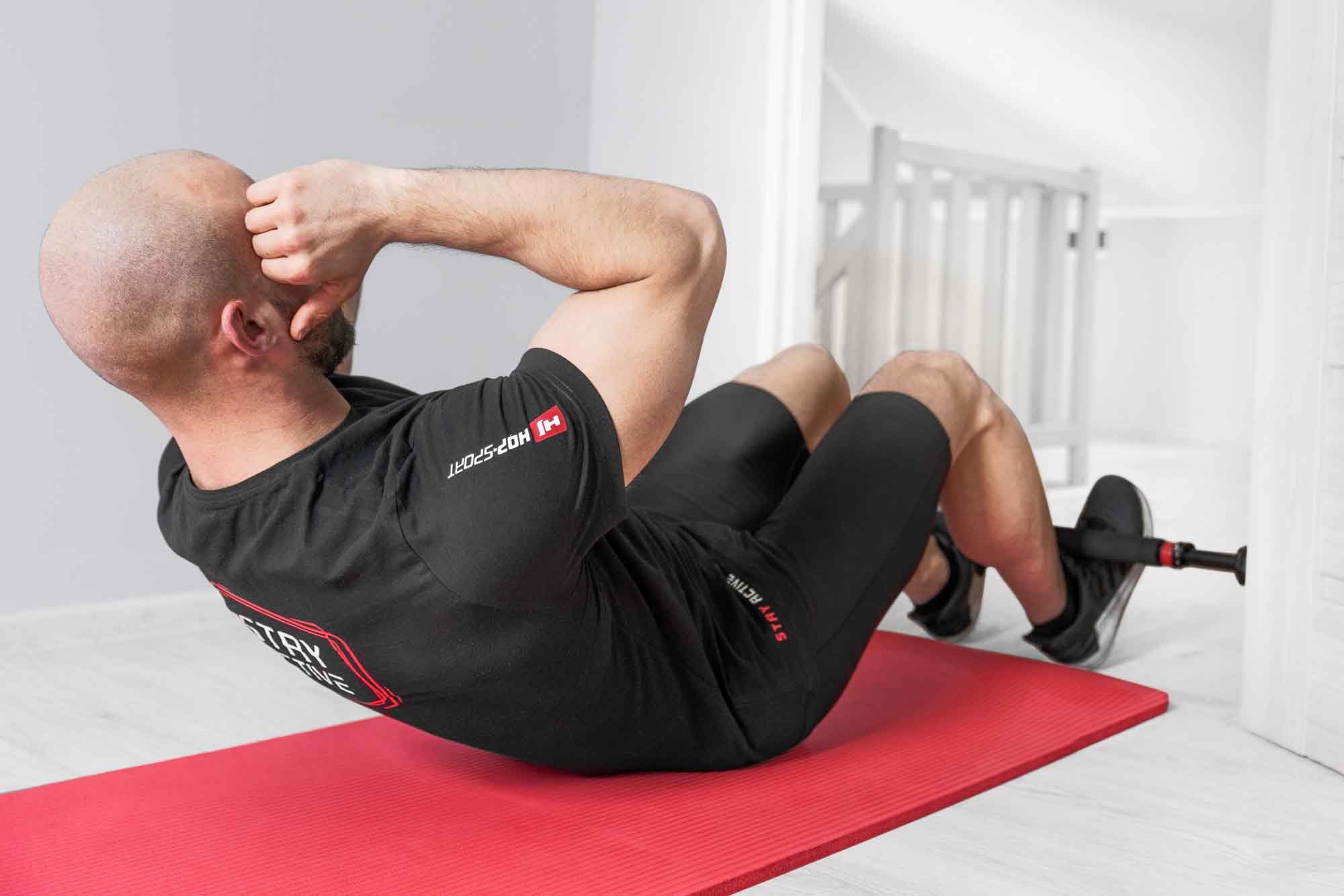 Ein glatzköpfiger Mann macht Sit-ups auf einer roten Matte mit fixierten Füßen.