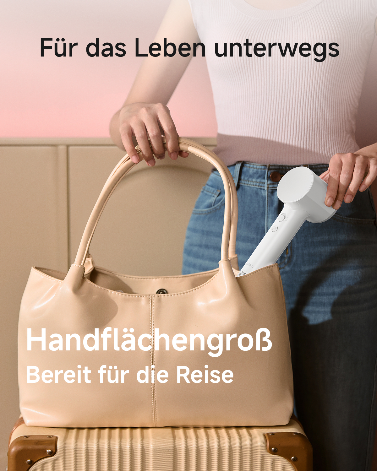 Eine Frau packt einen kleinen weißen Haartrockner in eine beige Handtasche vor einem rosafarbenen Hintergrund.