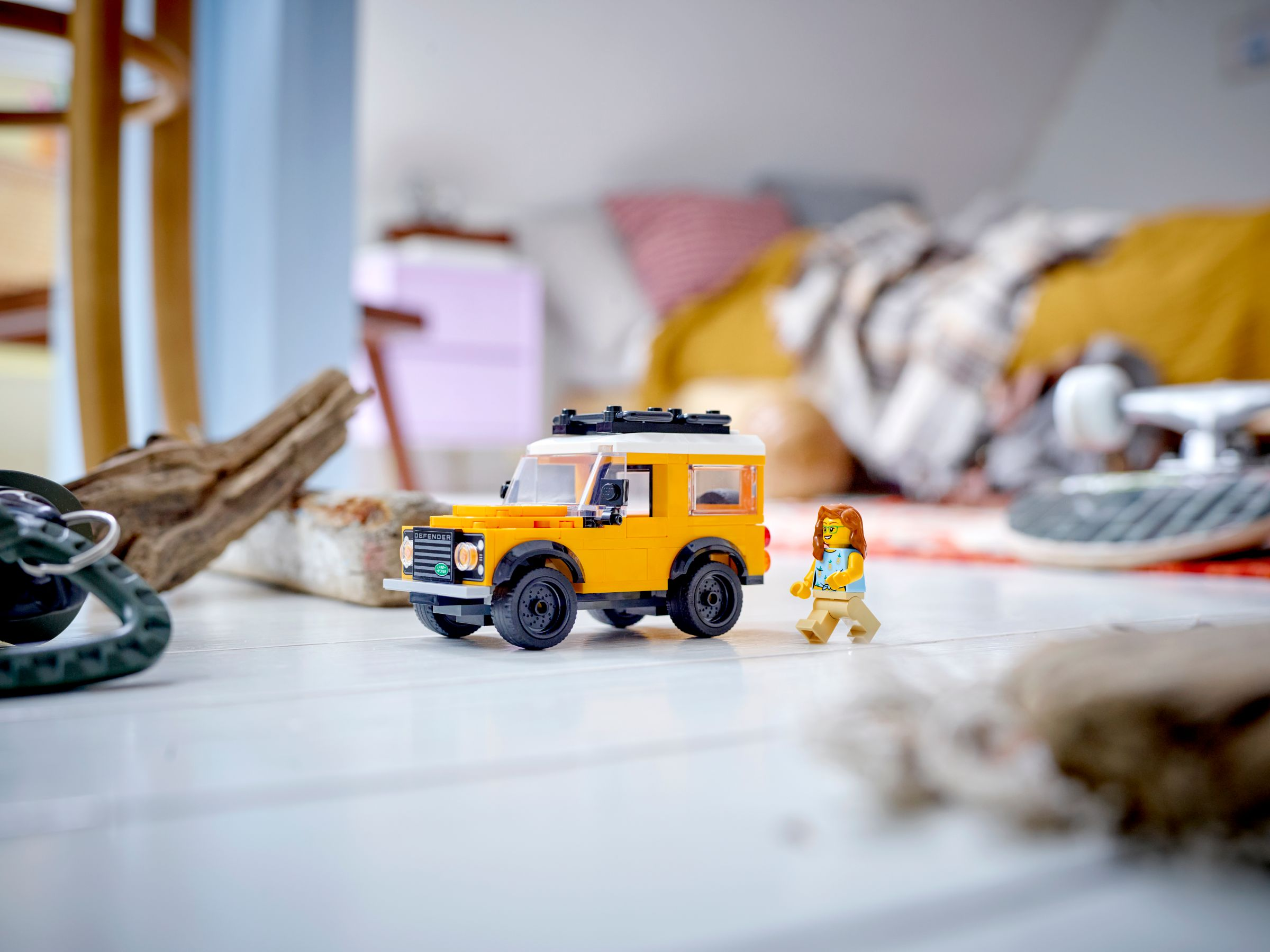 Ein kleines gelbes Lego-Auto und eine Lego-Figur stehen auf einem weißen Holzboden im Zimmer.
