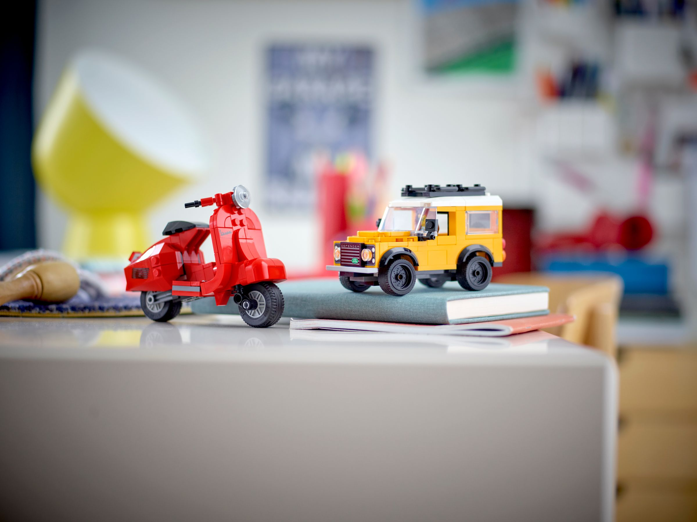 Ein roter Lego-Roller und ein gelber Lego-Jeep stehen auf einem Buch auf einem Tisch.