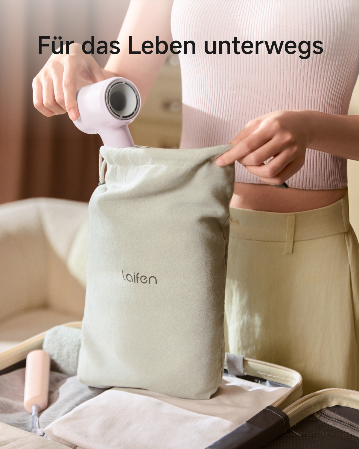 Eine Frau packt einen rosa Haartrockner in eine hellgrüne Reisetasche in einem offenen Koffer.