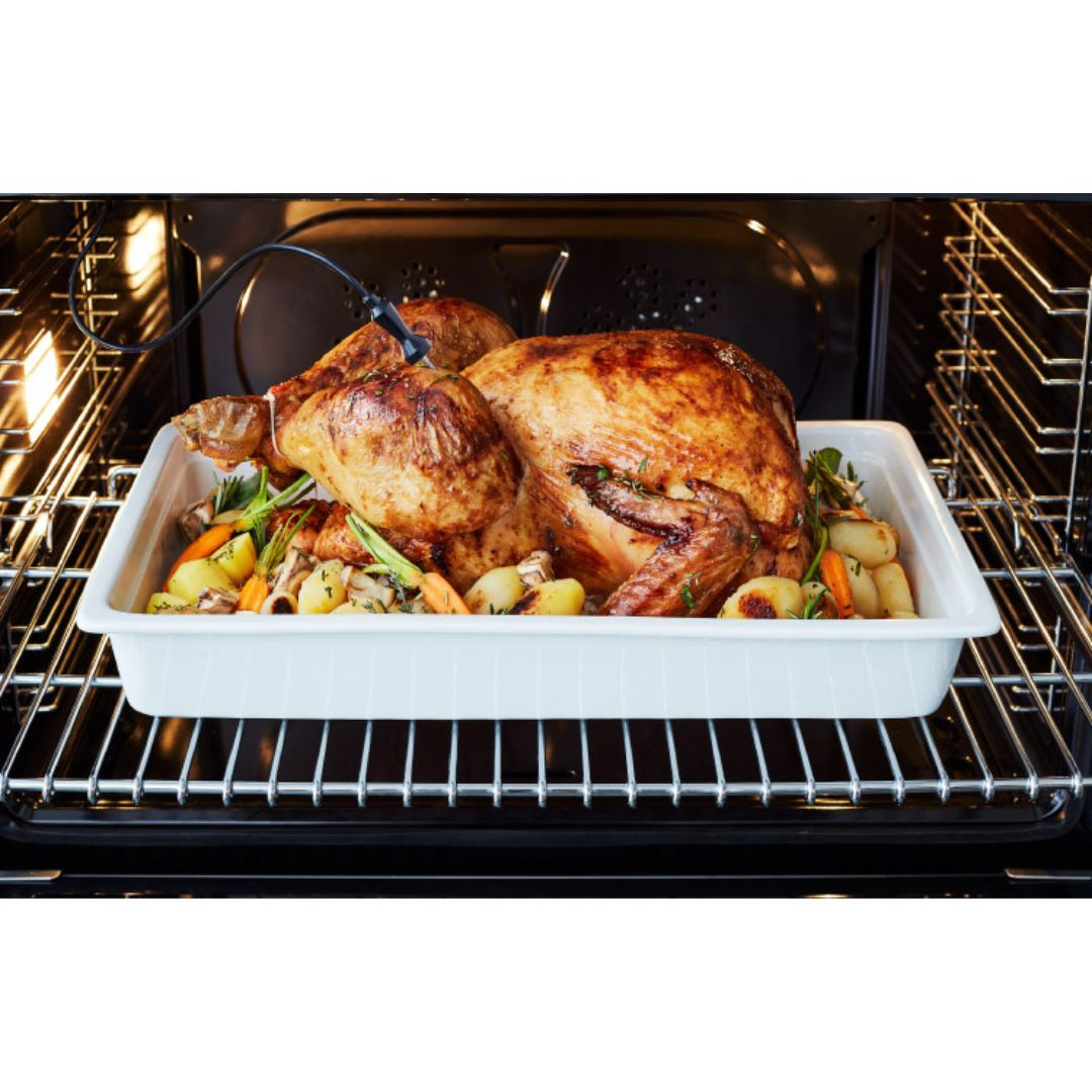 Un tacchino arrosto dorato con verdure in una teglia da forno, con una sonda per carne.