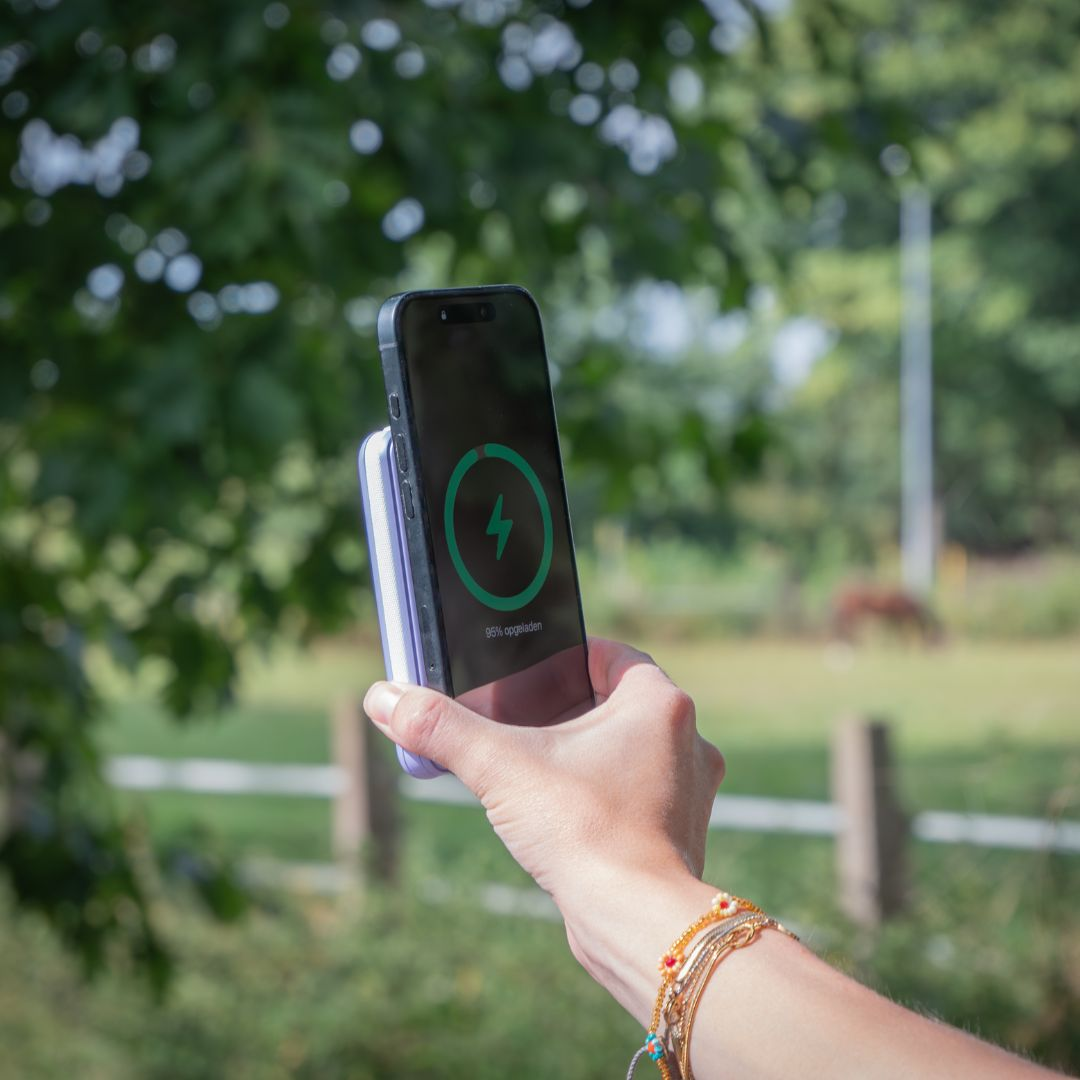 Eine Hand hält ein Smartphone mit grünem Ladekreis vor verschwommenem grünen Park.