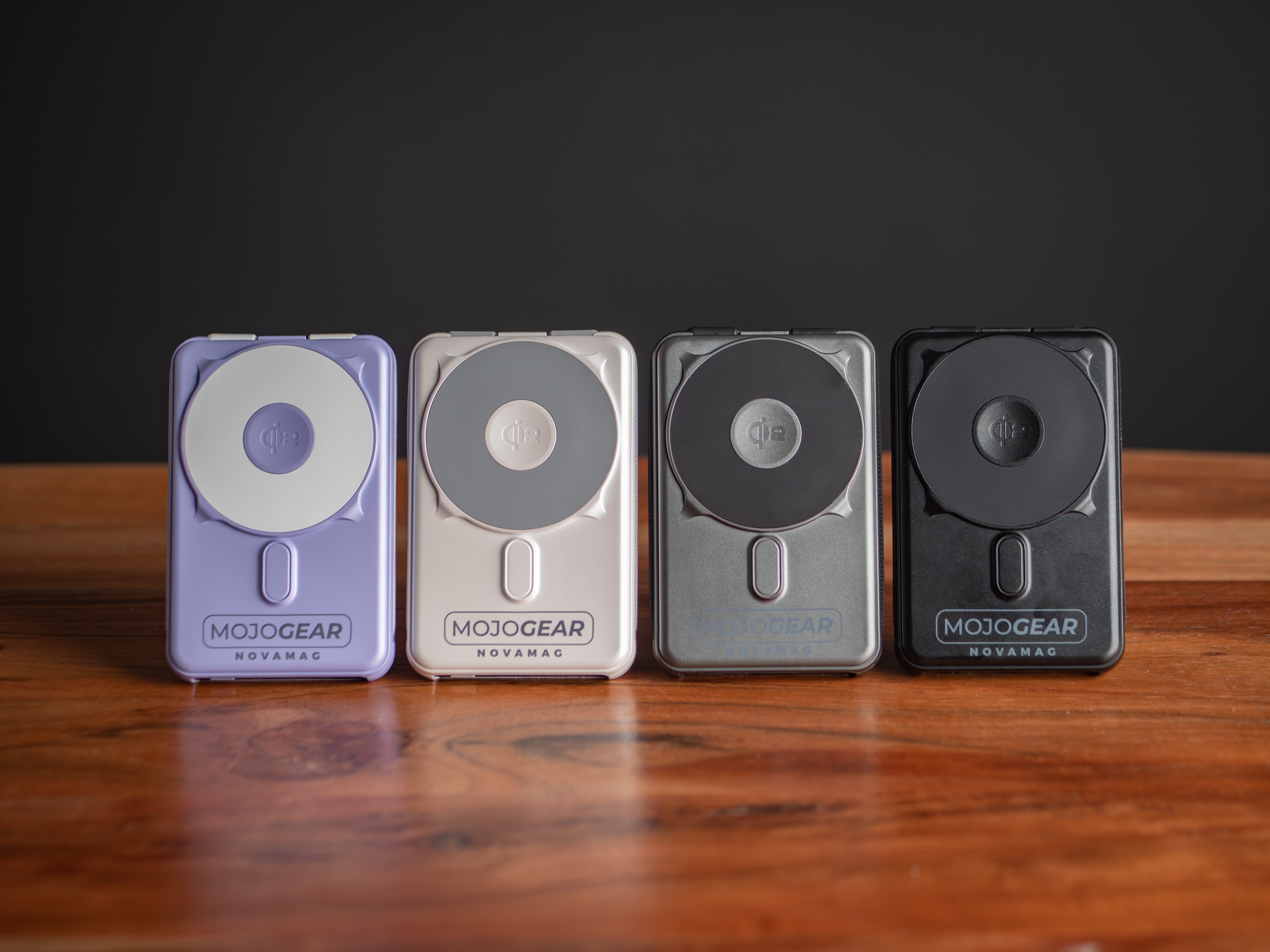 Vier Mojogear Novamag Powerbanks in Lila, Silber, Grau und Schwarz stehen nebeneinander auf einer Holzoberfläche.