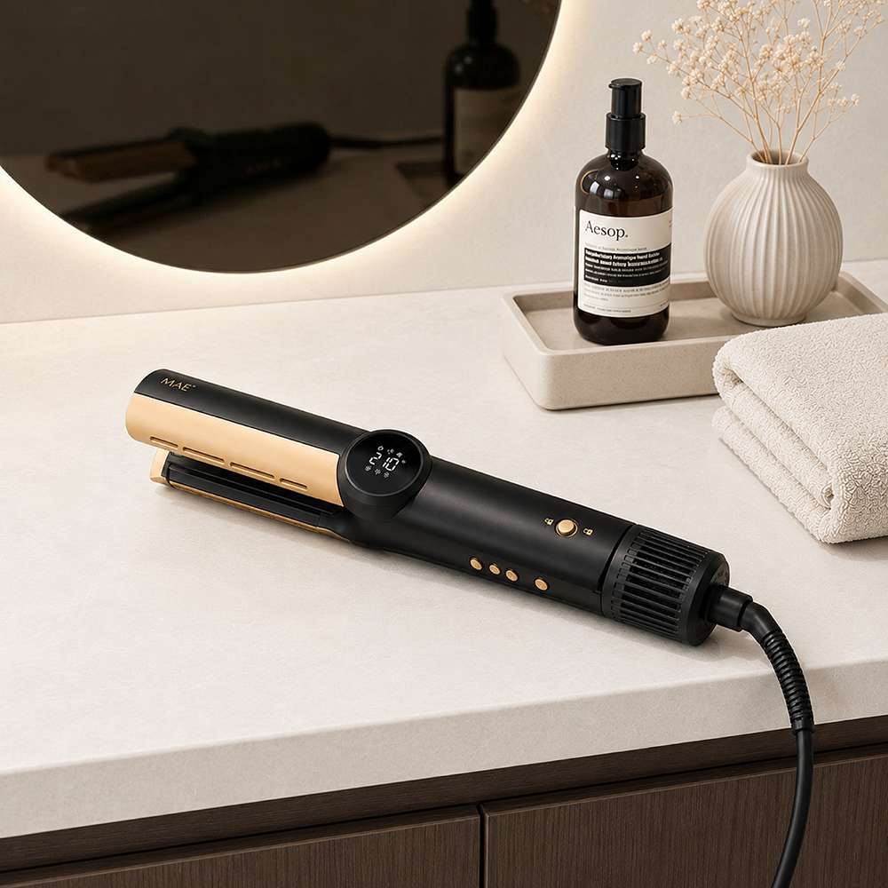 A black and gold hair straightener on a white countertop next to a mirror and a soap bottle.