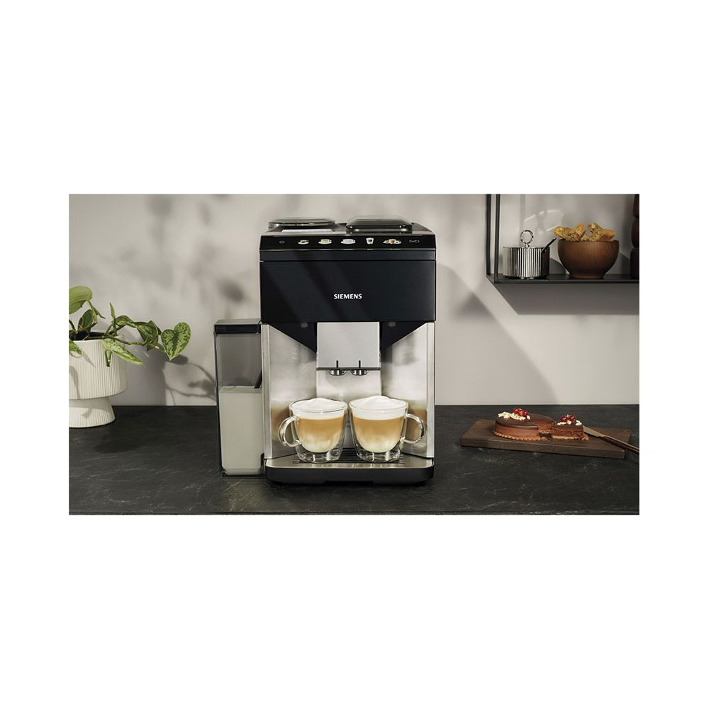 Una macchina da caffè Siemens prepara due cappuccini su un bancone scuro accanto a una torta e una pianta.