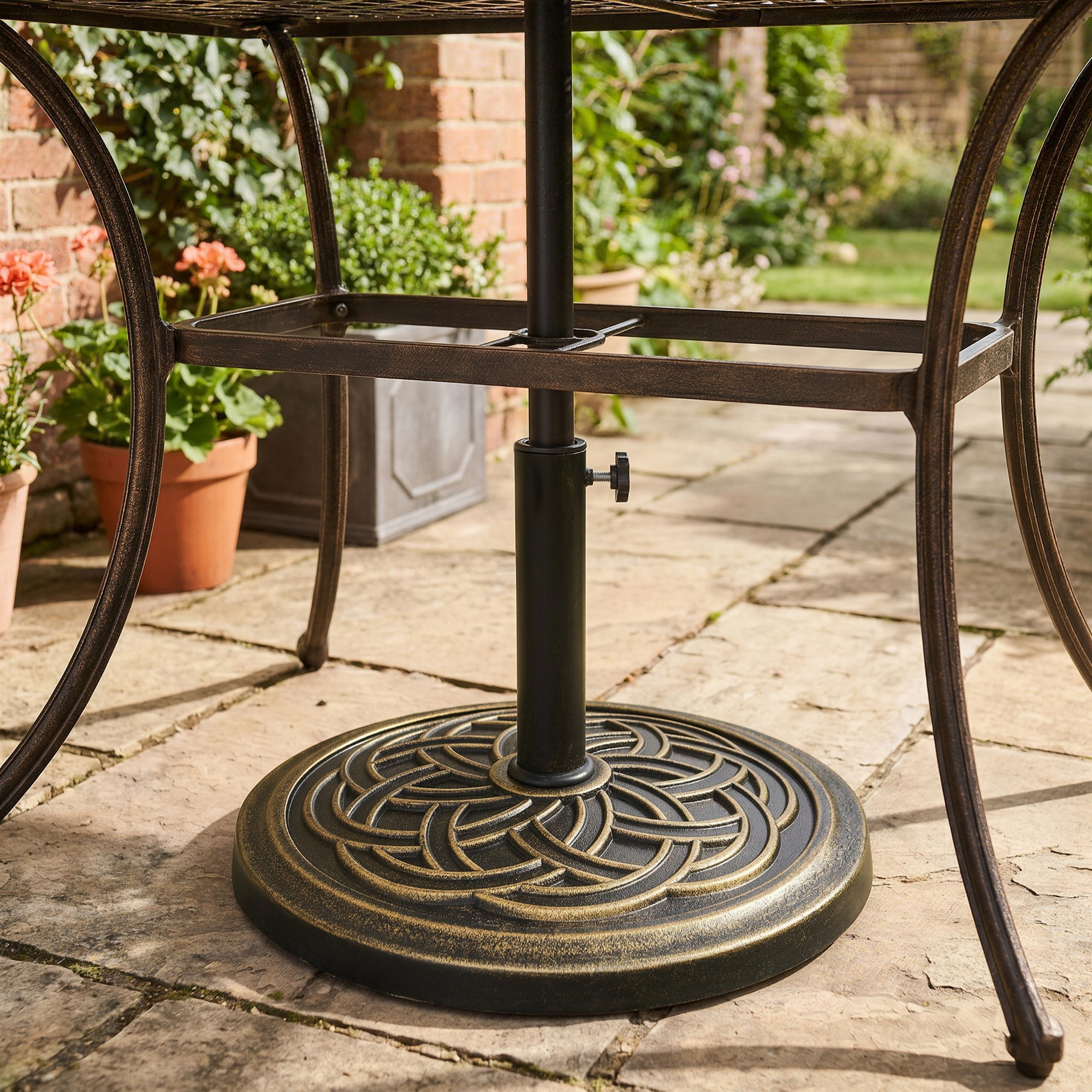 Primer plano de una base de mesa de exterior de bronce en un patio de piedra con plantas en maceta.