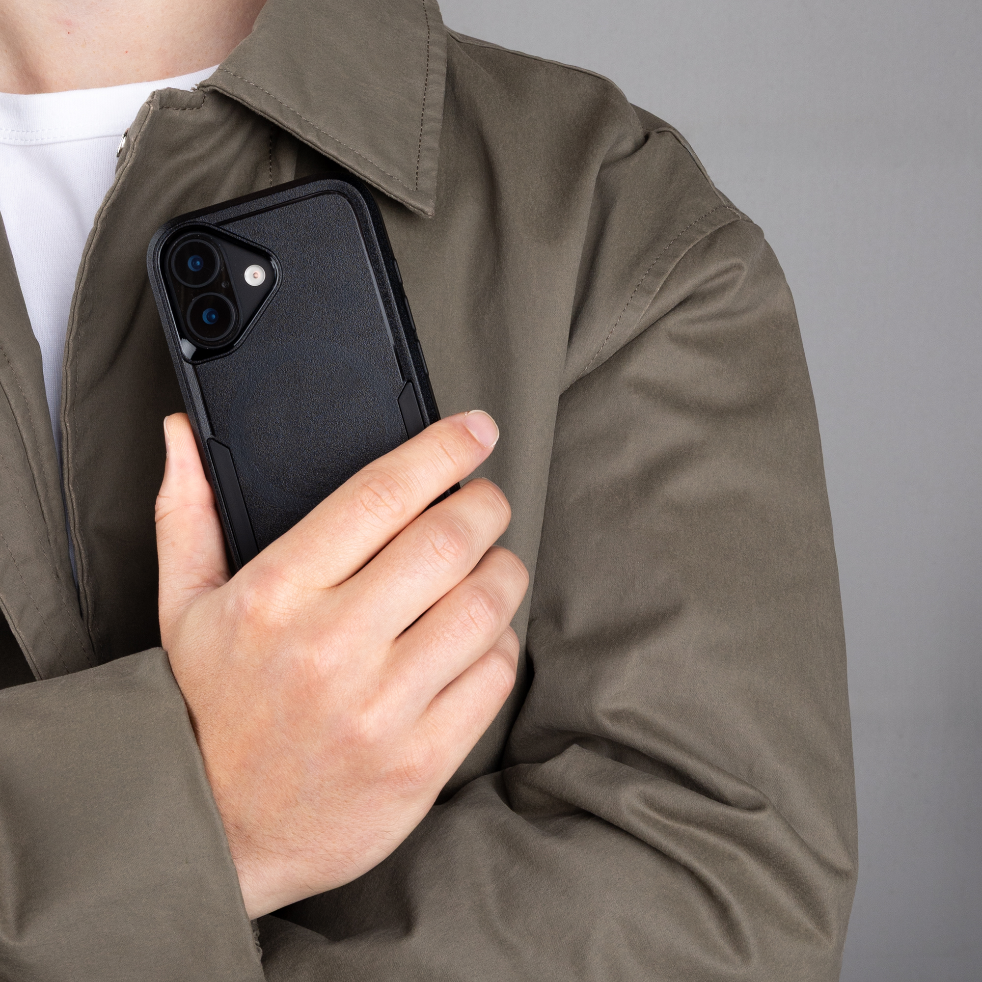 Iemand in een groene jas houdt een zwarte smartphone in een beschermhoes tegen de borst.