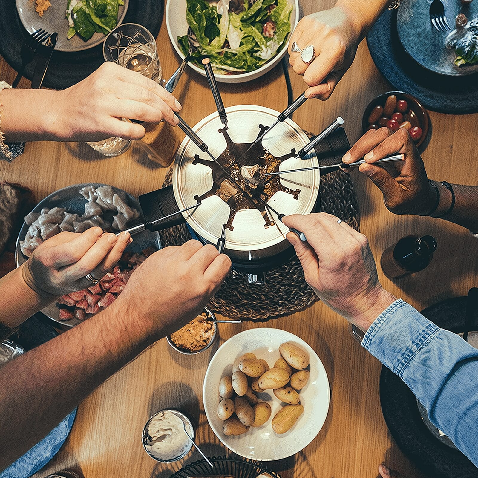 Draufsicht von Personen, die Essen in einen zentralen Fonduepott tauchen.