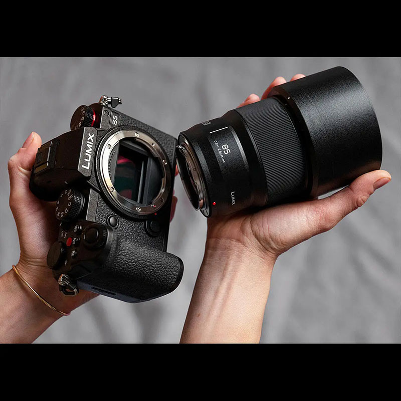 Des mains tenant un boîtier de caméra noir Lumix S5 et un objectif.