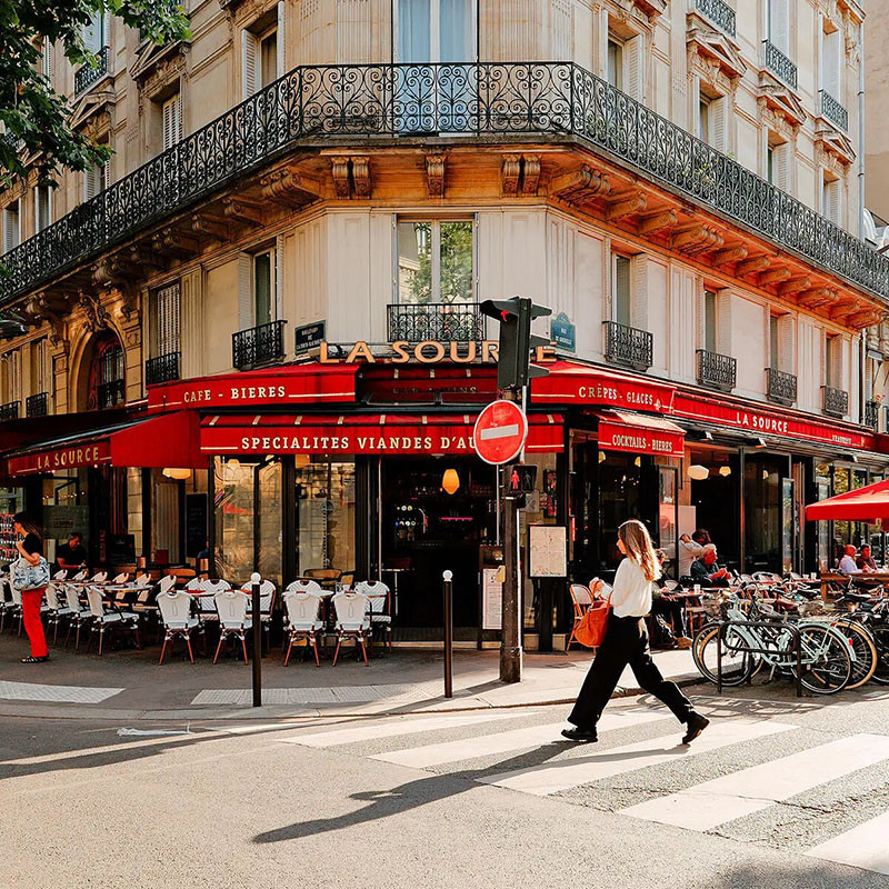 Una donna cammina davanti a un bar d'angolo con tende rosse a Parigi.