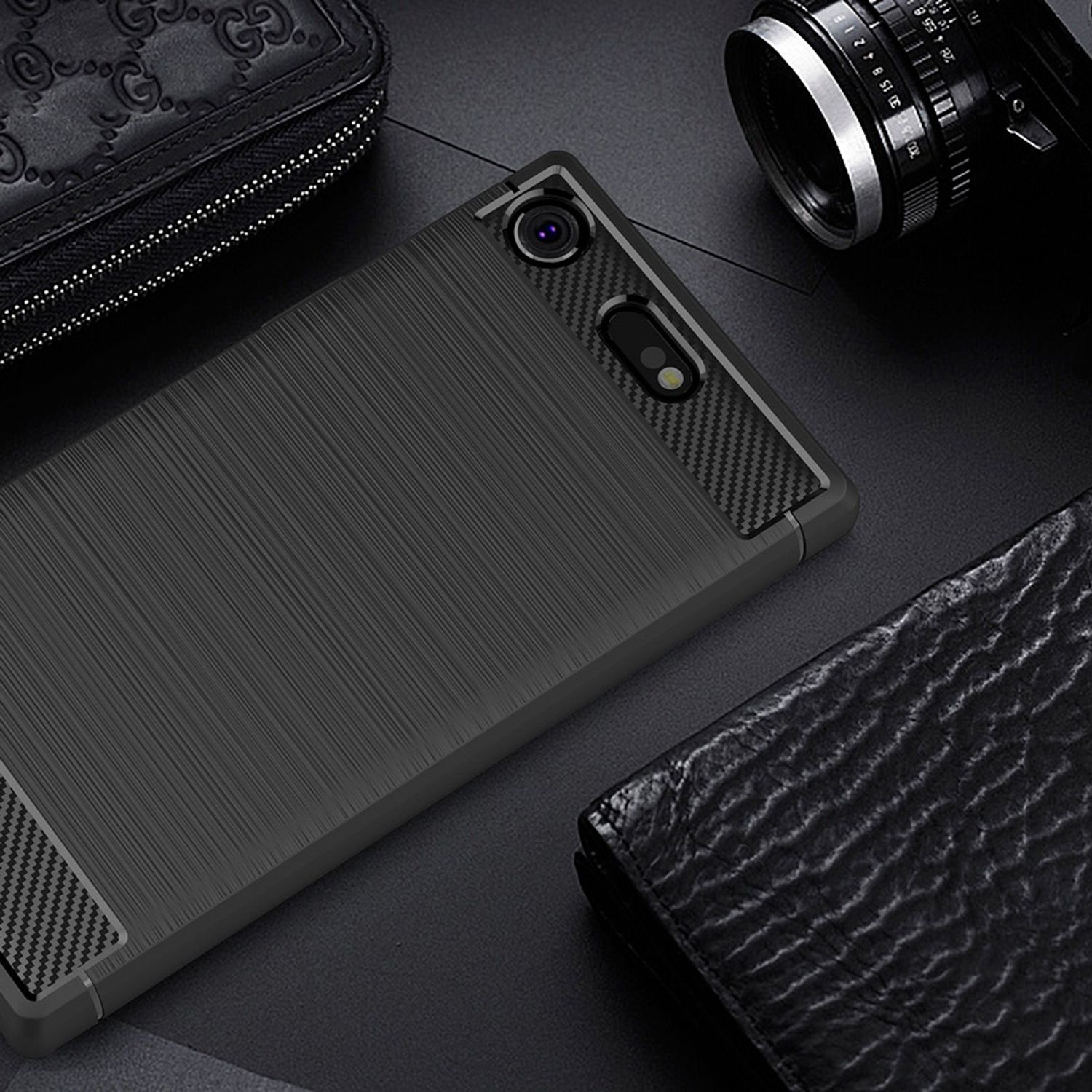 Un teléfono negro con textura cepillada sobre fondo oscuro, rodeado de artículos de cuero y una cámara.