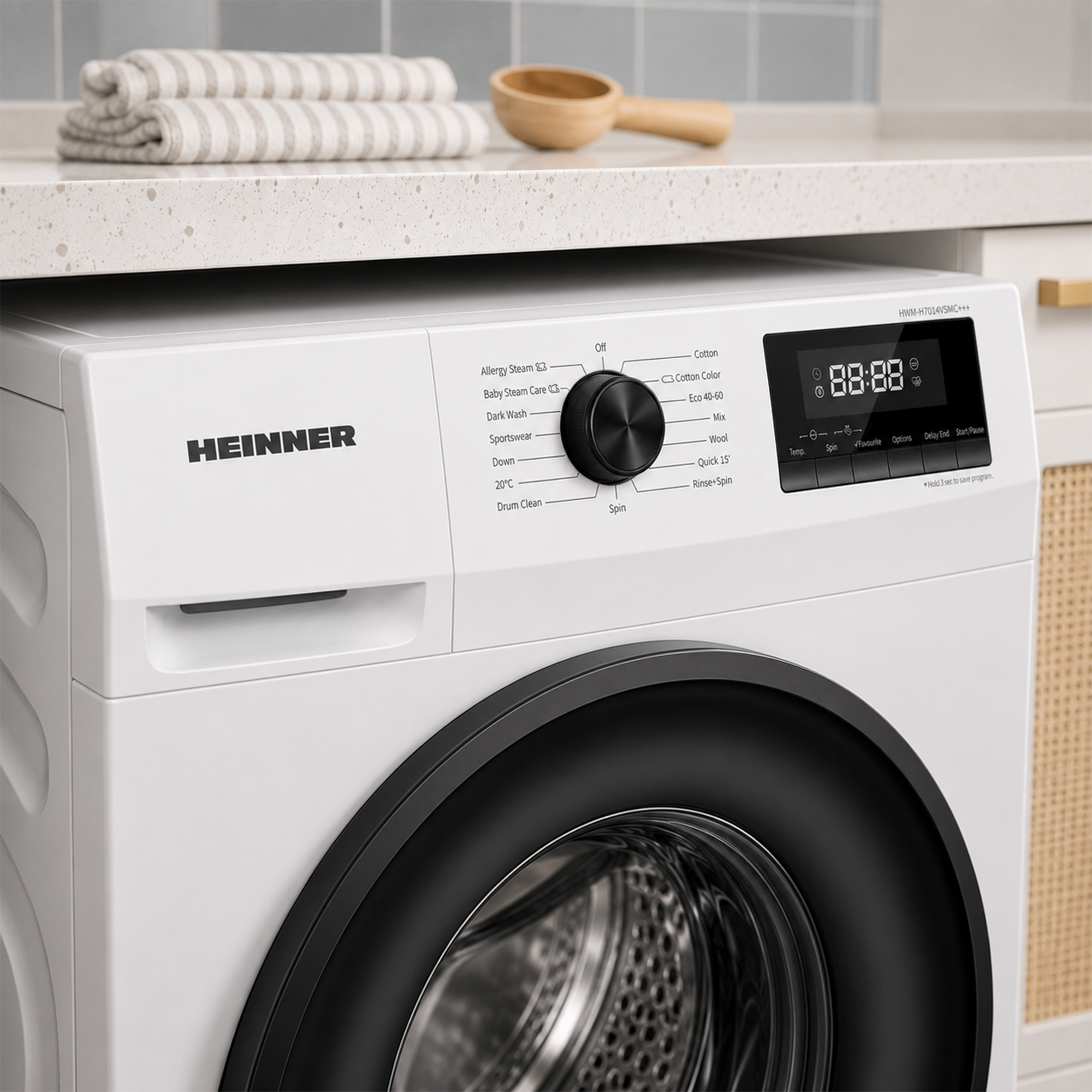 Un lave-linge blanc Heinner sous un comptoir avec des serviettes pliées et une cuillère en bois.