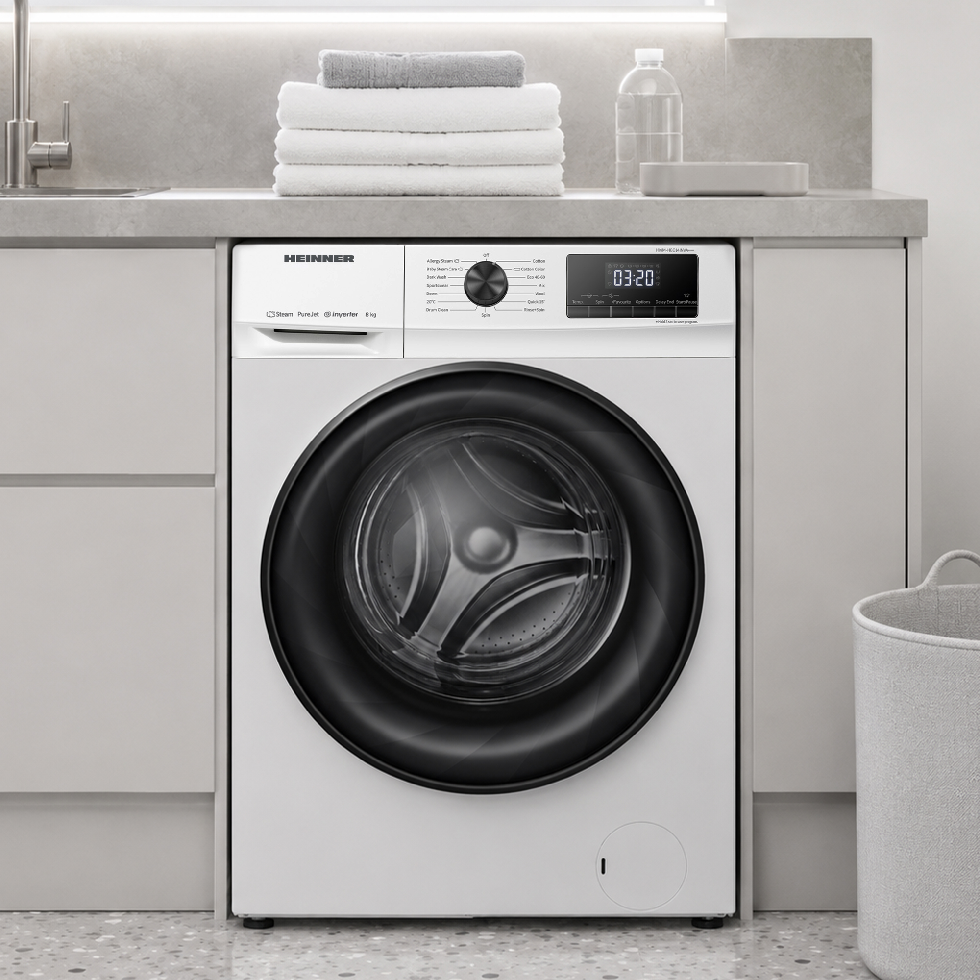 Un lave-linge blanc Heinner est placé sous un comptoir avec des serviettes empilées et une bouteille.