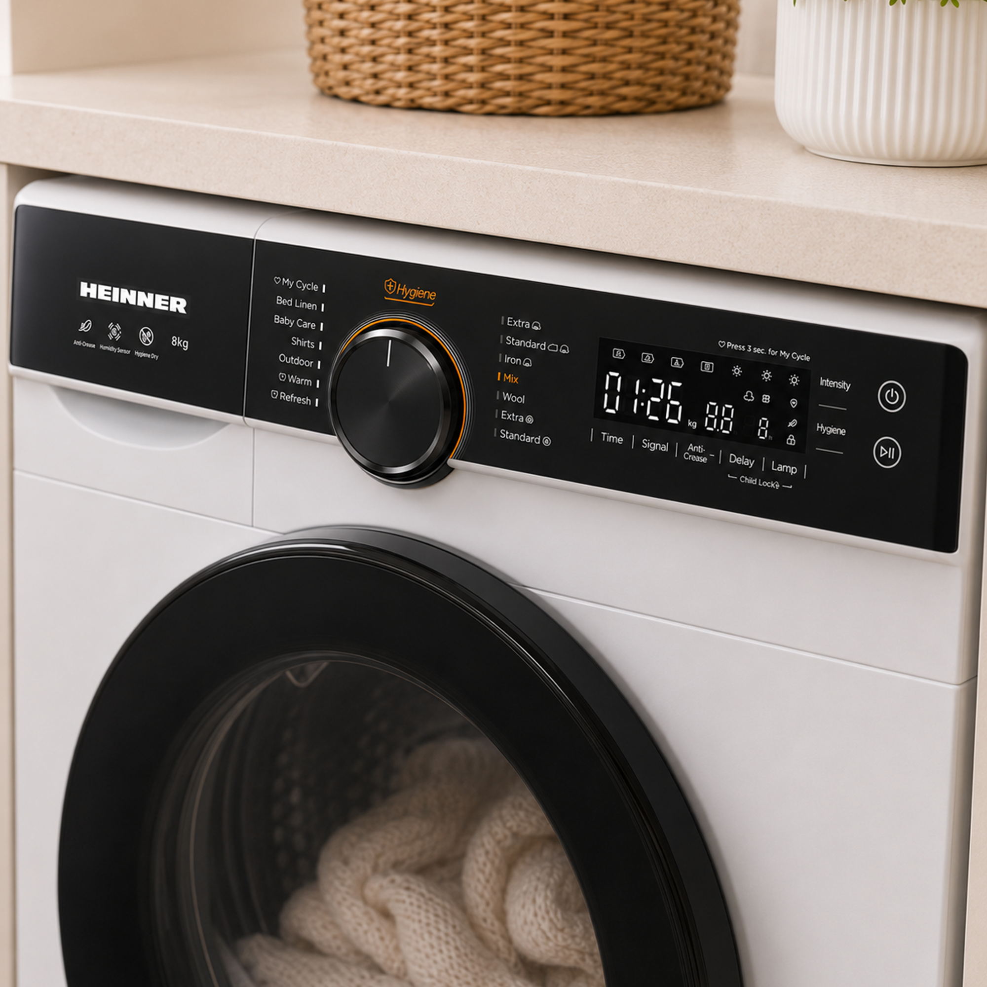 Witte Heinner wasmachine met zwart bedieningspaneel en ronde deur. Een mand en plant staan op het aanrecht.
