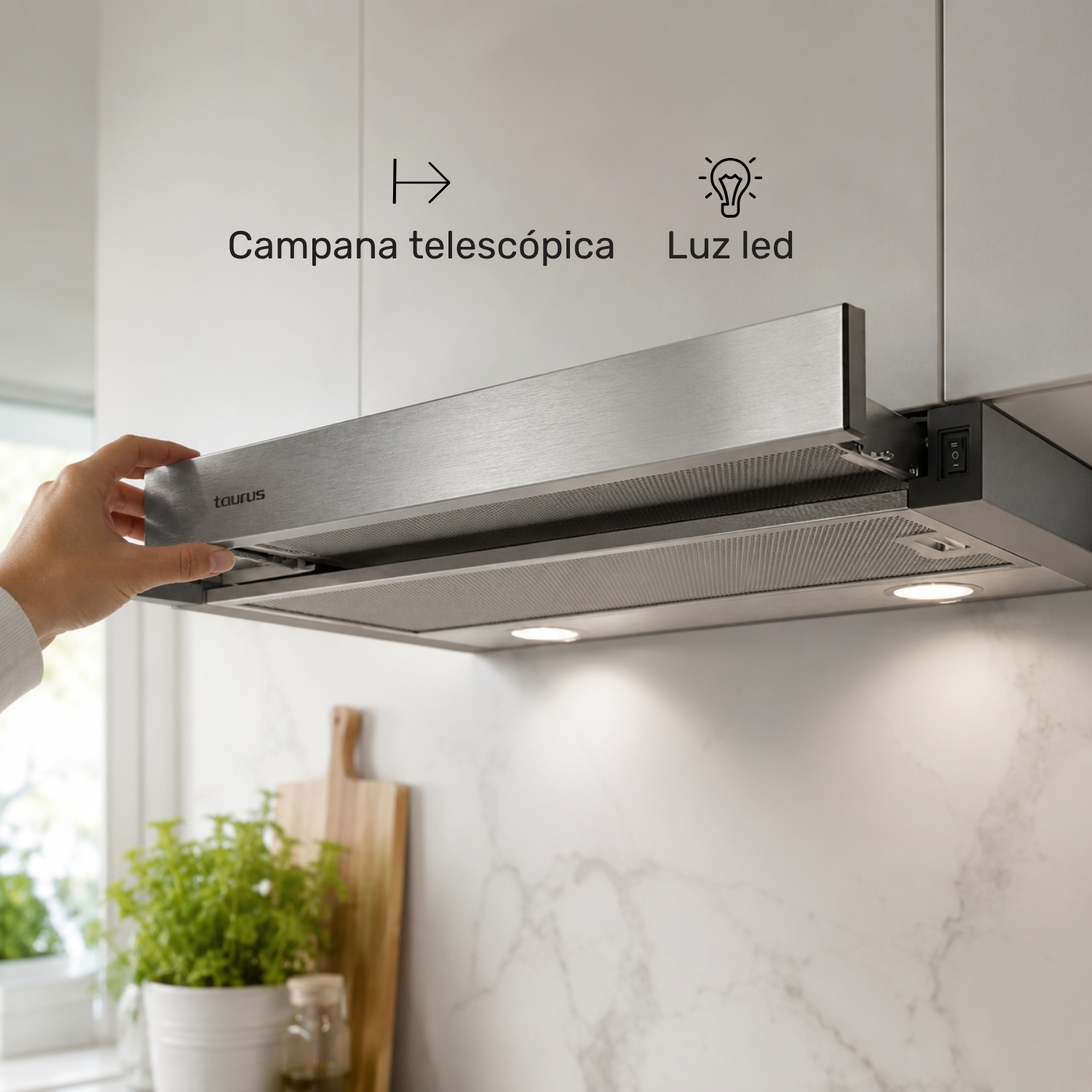 Una mano extrae una campana extractora telescópica Taurus plateada bajo los armarios.