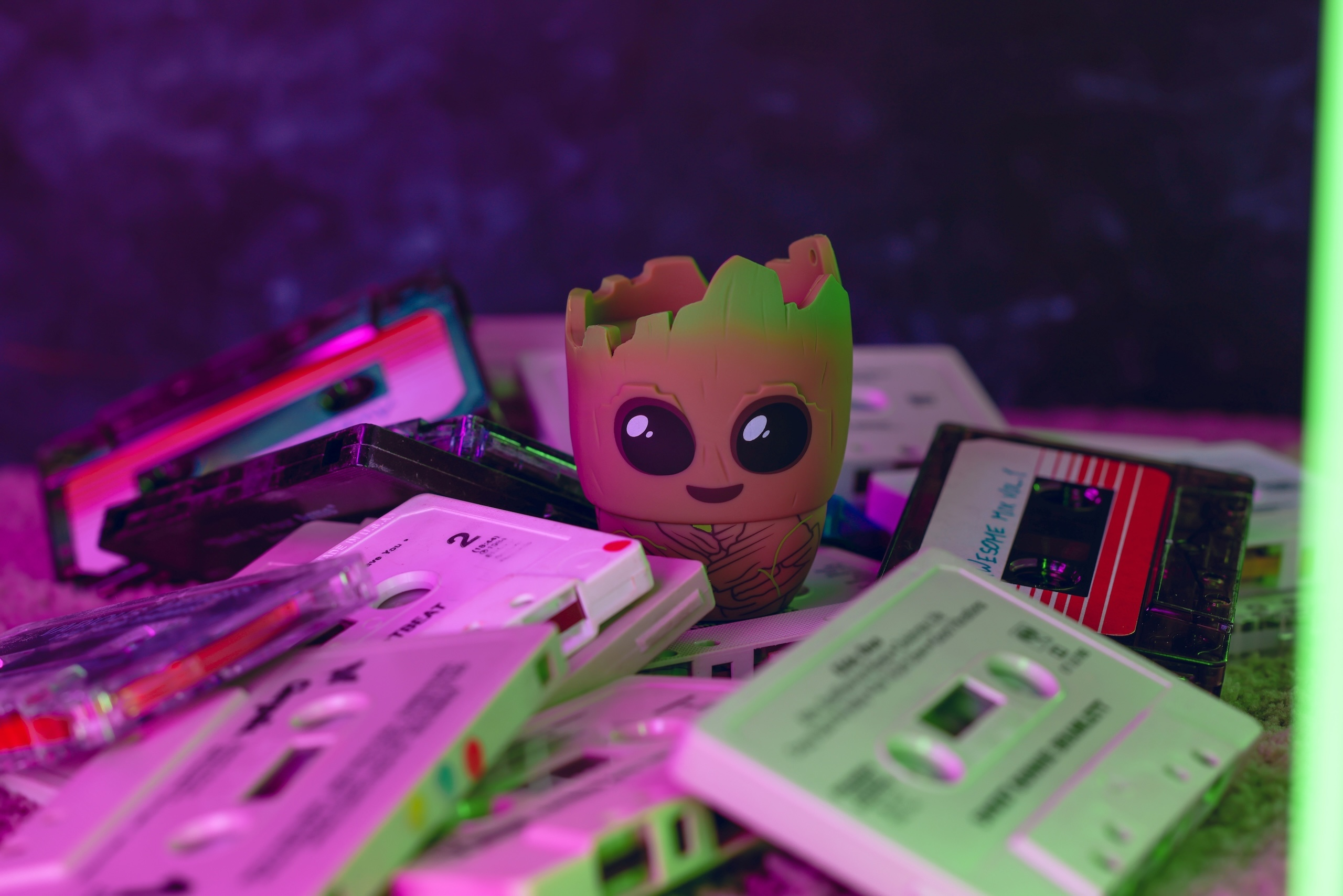 Una piccola statuetta di Baby Groot si trova in mezzo a un mucchio di cassette colorate e bianche sotto la luce al neon.