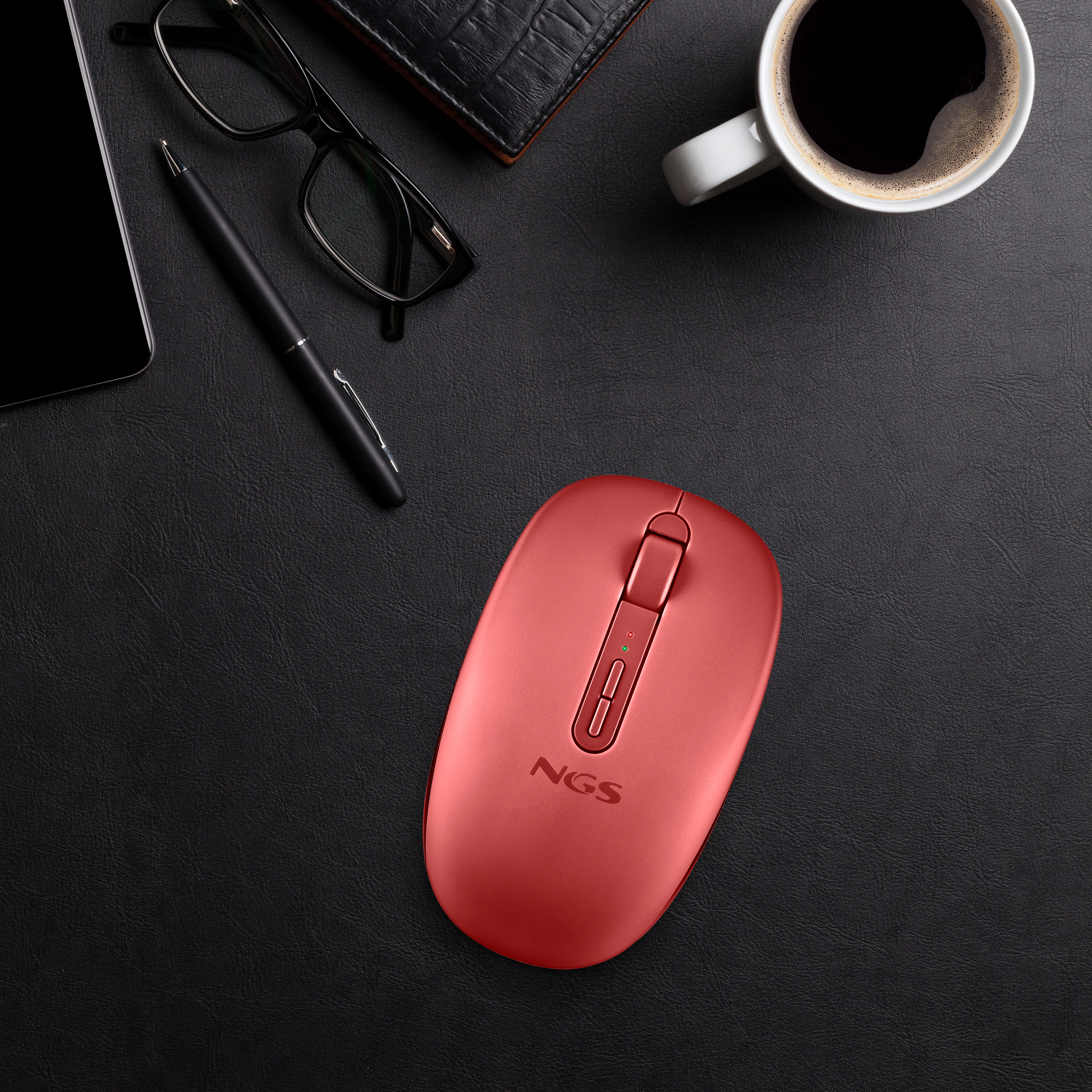 Un mouse wireless NGS rosso su una scrivania in pelle nera con telefono, occhiali, penna, portafoglio e caffè.