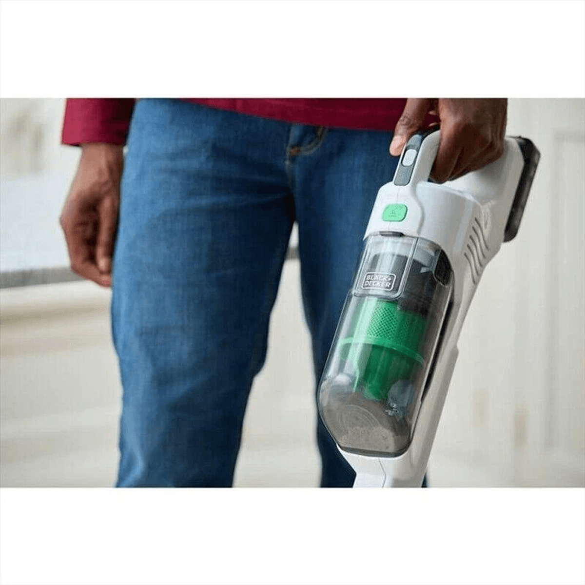 Una persona con jeans blu tiene in mano un aspirapolvere portatile bianco e verde.