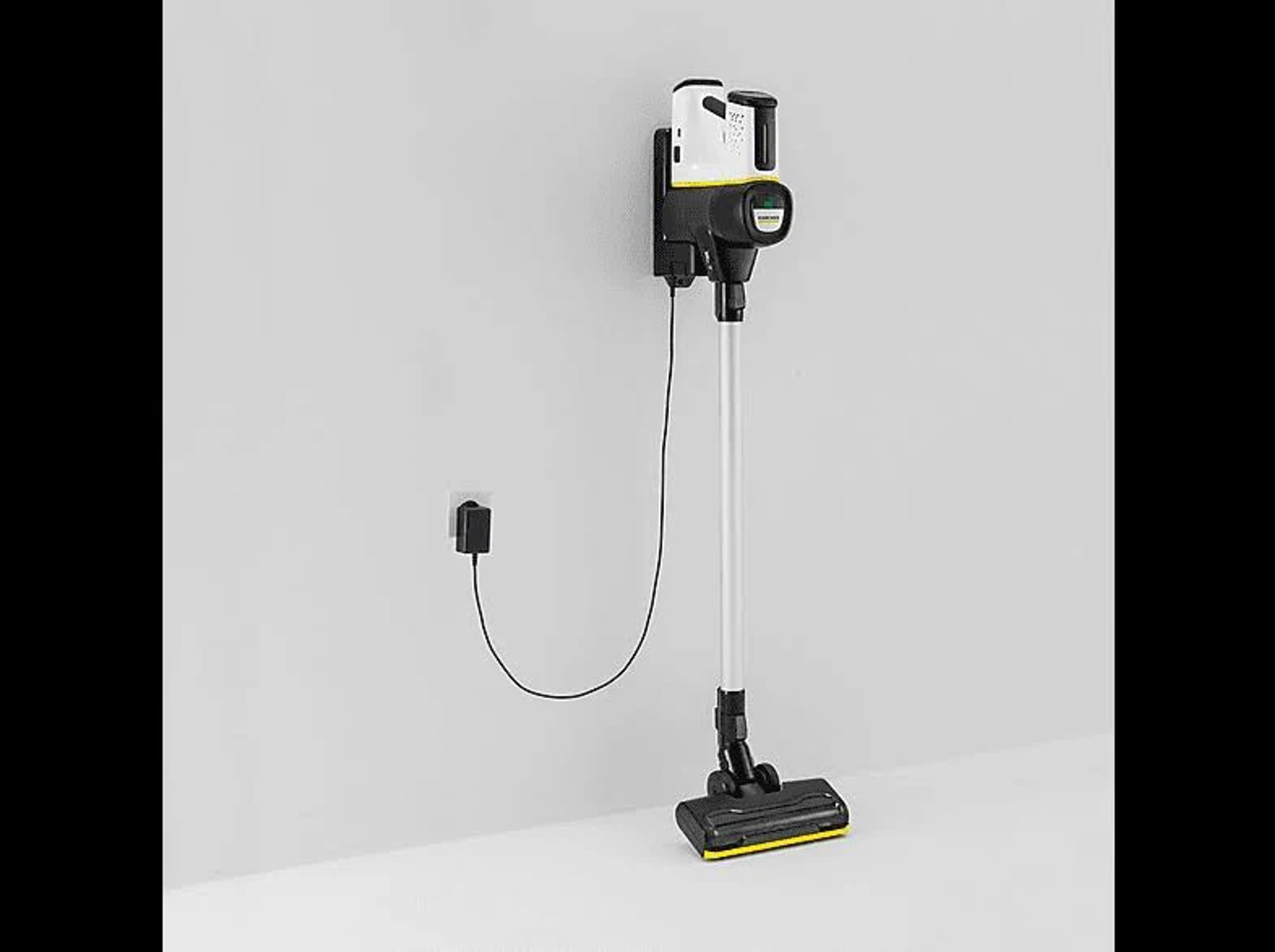 Un aspirateur blanc et noir est fixé au mur et branché sur une prise électrique.