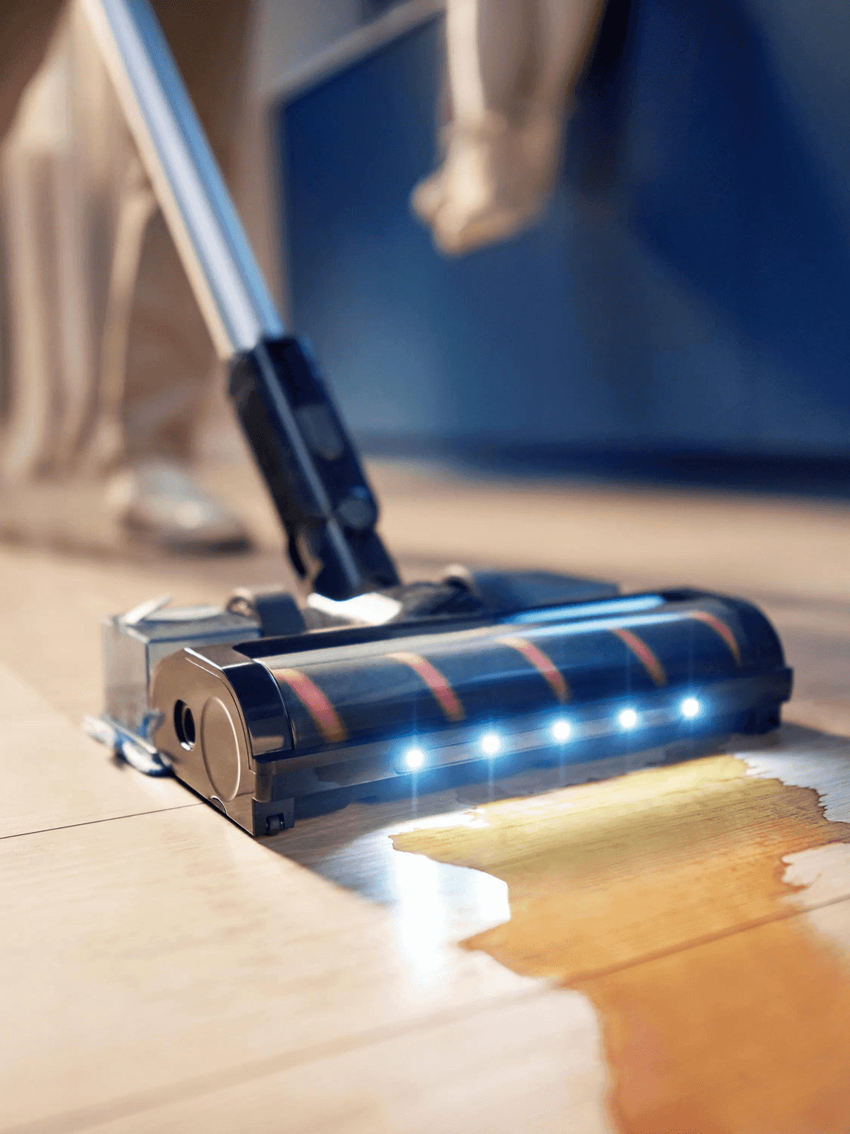 Un aspirapolvere senza fili per solidi e liquidi con LED blu pulisce un liquido versato su pavimento in legno.